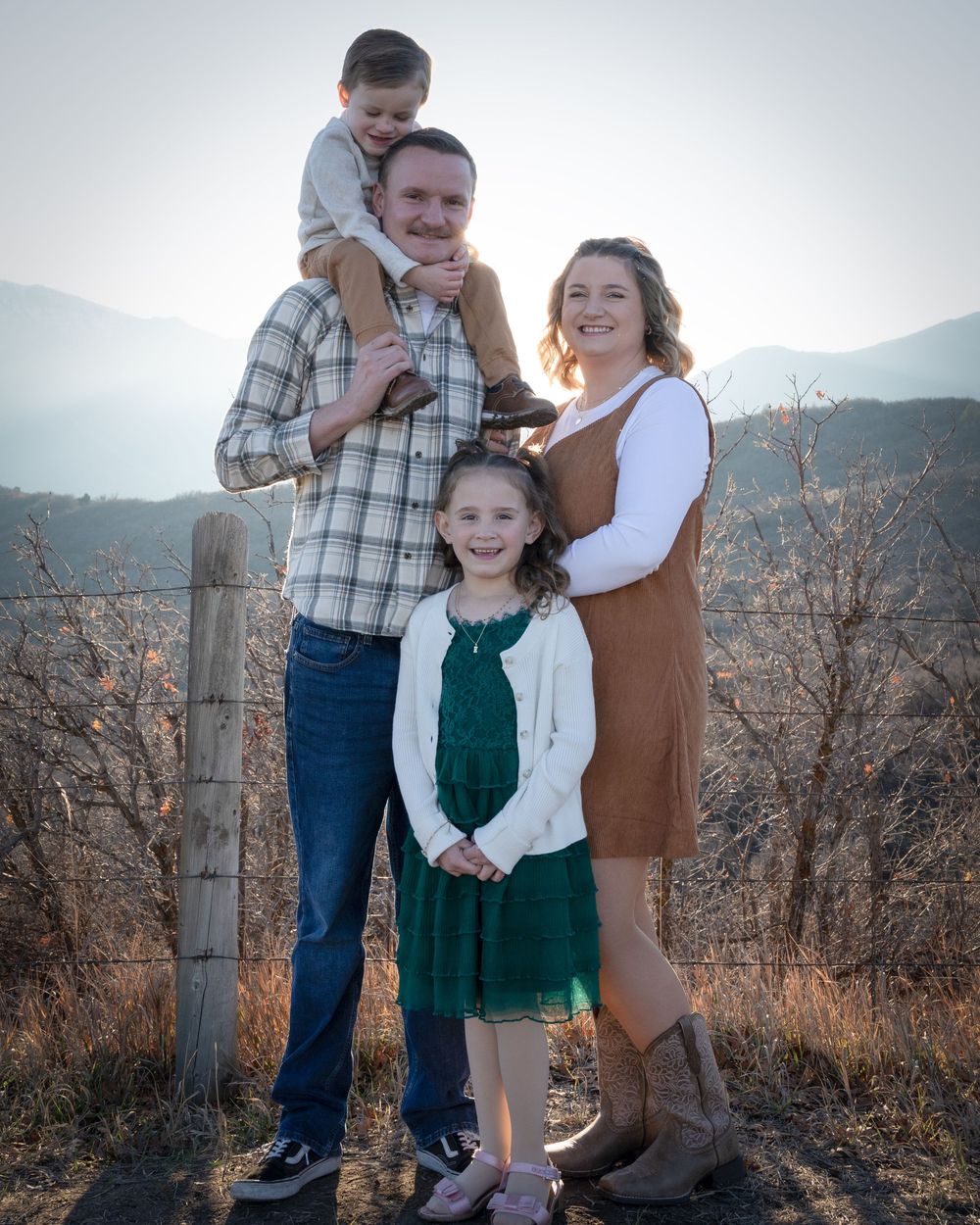 Family portrait with rustic mountain scenery featuring coordinated casual outfits in earth tones.