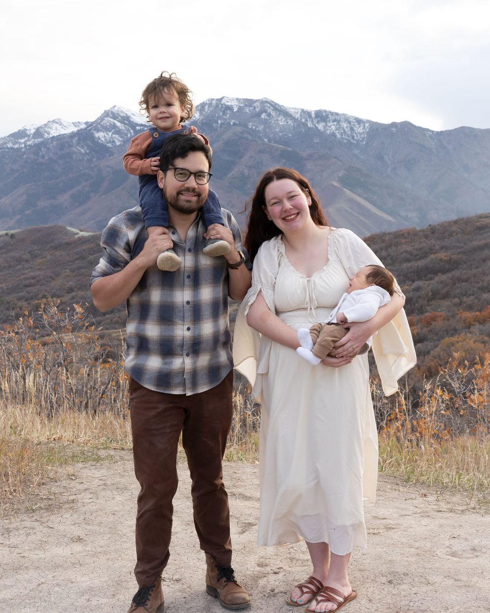 A couple poses together on a mountain trail with snow-capped peaks in the background.