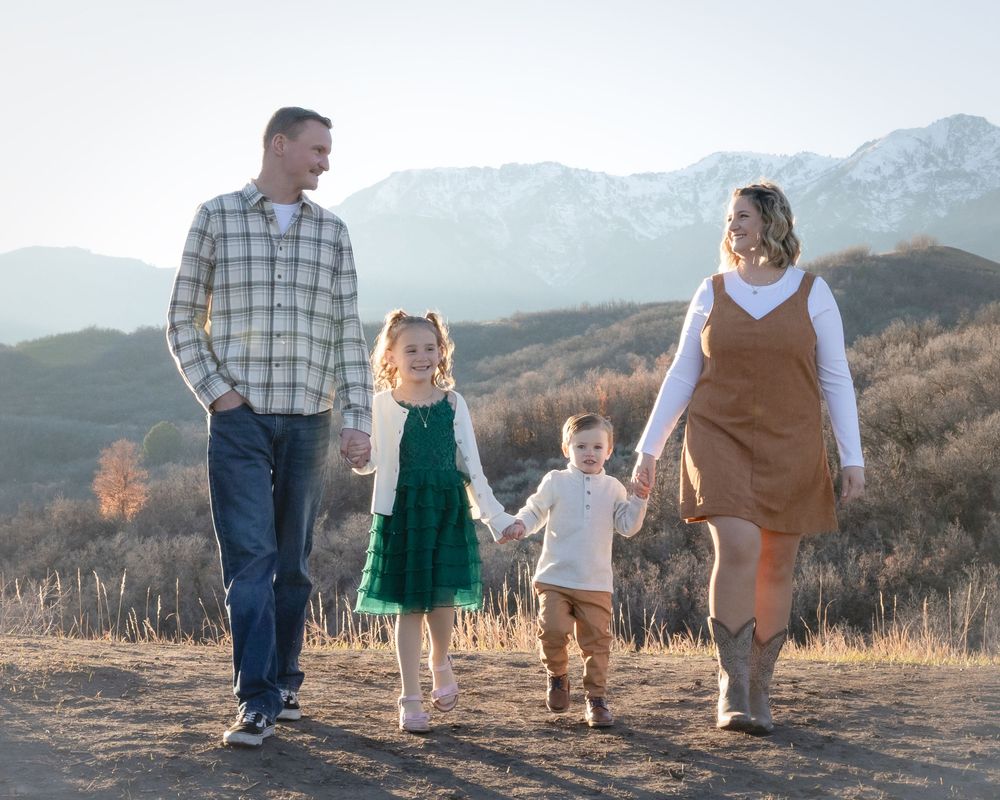 A family in coordinated outfits walks together on a mountain trail during golden hour sunset.