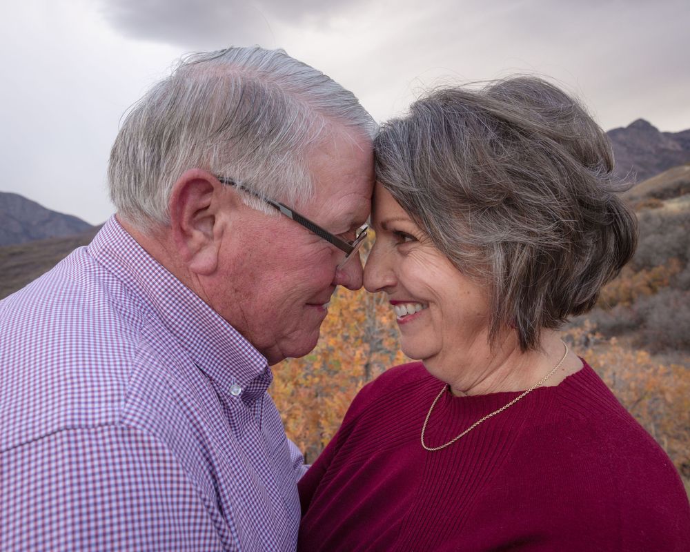 A couple in burgundy and purple plaid share tender moments against a scenic mountain backdrop at sunset.