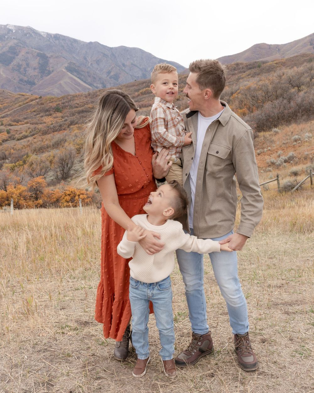 Family shares tender moments together in a rustic autumn field with mountains in the background.