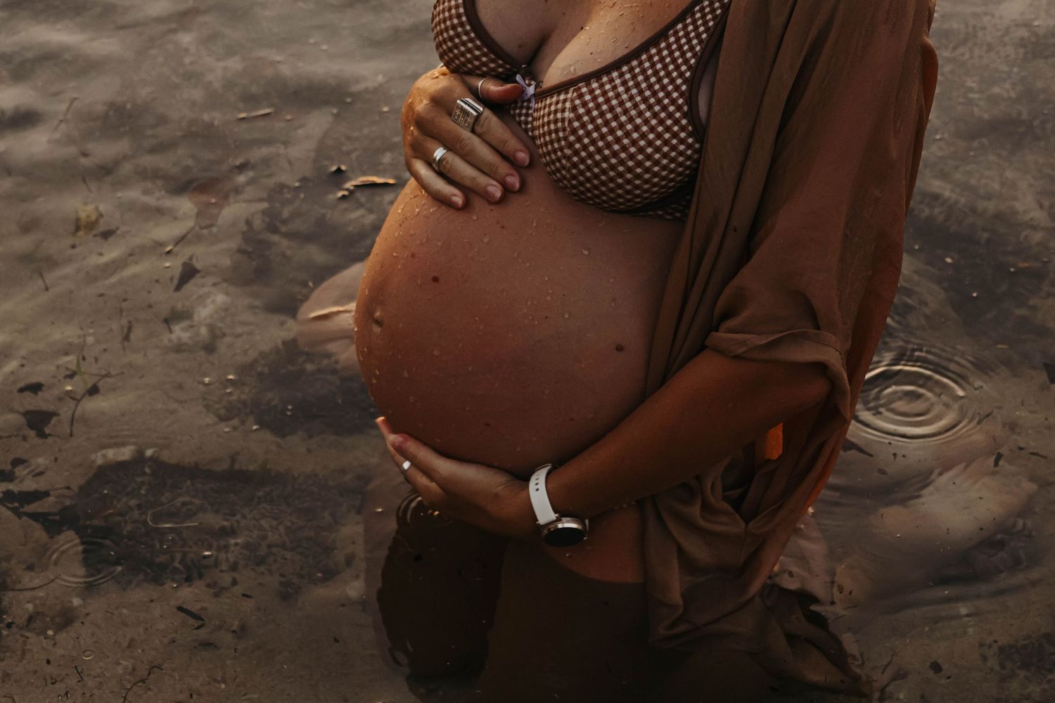 Close-up of pregnant woman in mesh bikini top cradling bare baby bump.