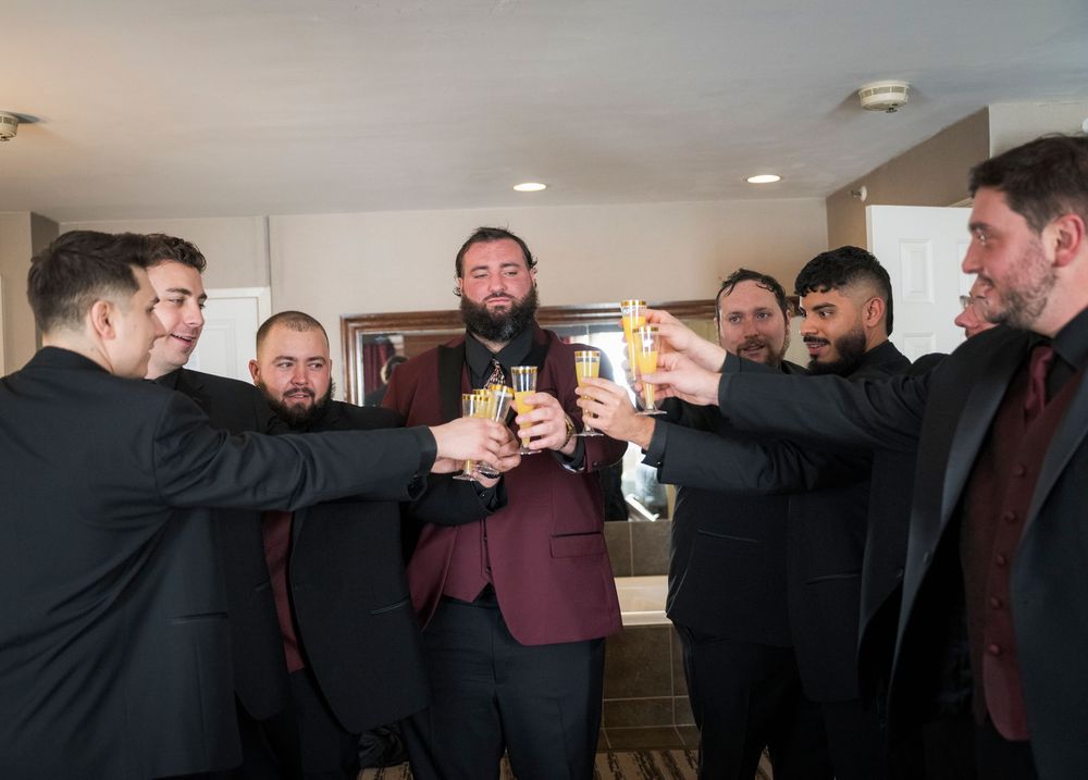 Groomsmen in dark suits sharing celebratory drinks before the wedding ceremony.