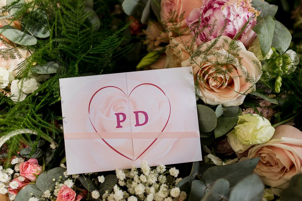 Pink heart-shaped wedding card with initials PD surrounded by roses and baby's breath flowers.