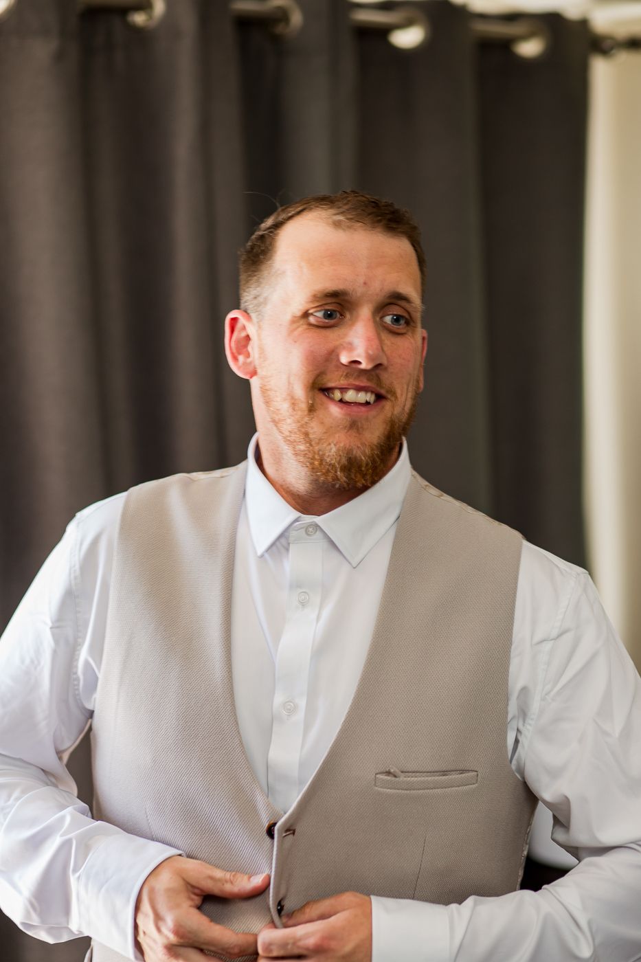 Groom in white shirt and light gray vest during wedding preparations.
