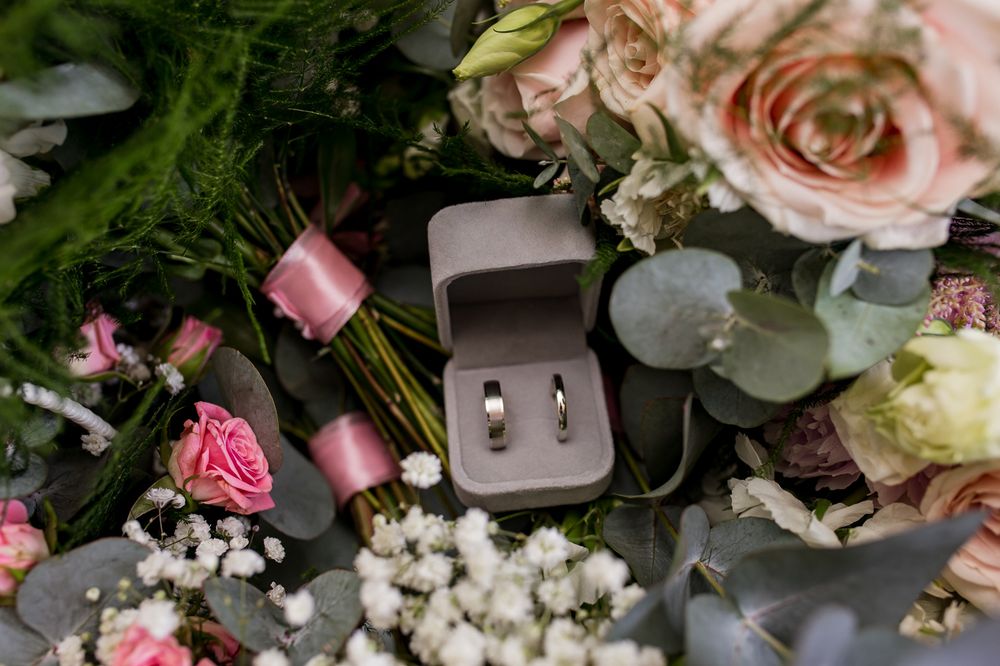 Wedding rings in a gray box nestled among pink roses, eucalyptus leaves, and baby's breath flowers.