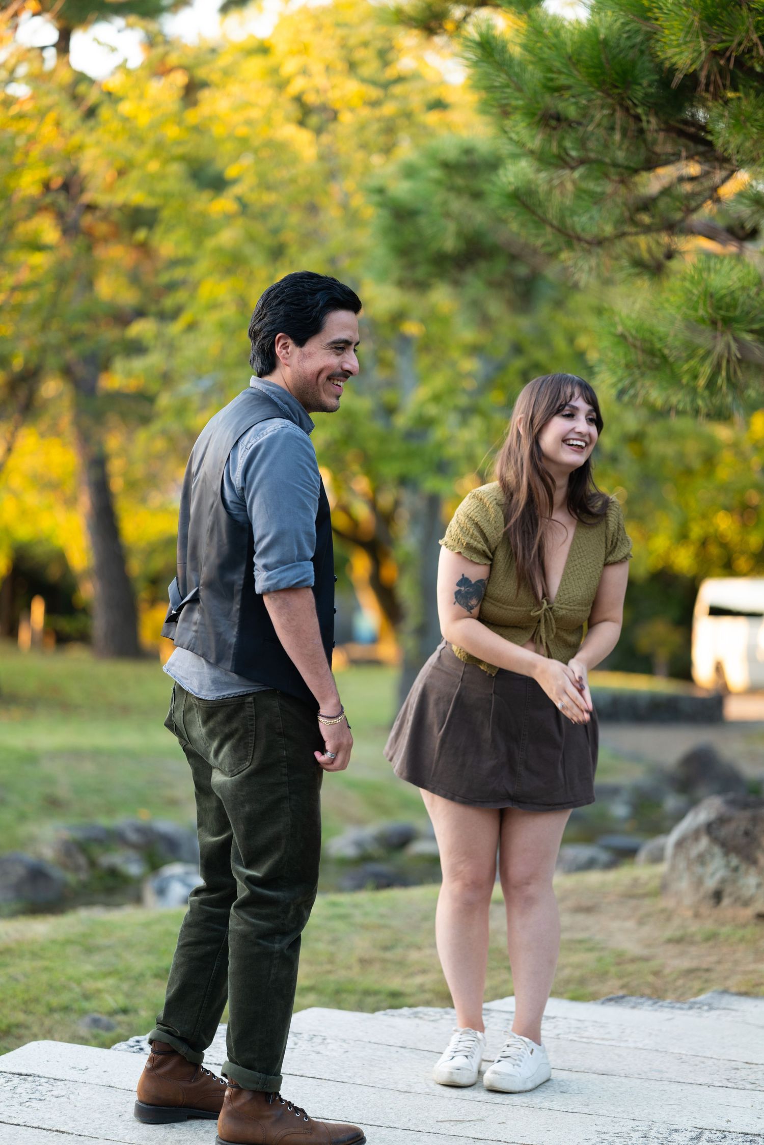 Happy couple laughing together on a stone path in a sunlit autumn park.