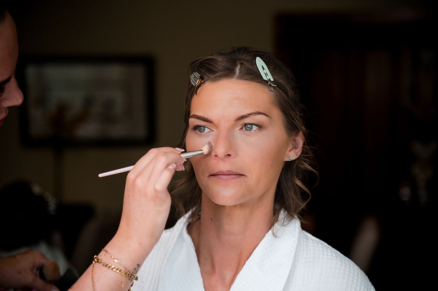 Person applying makeup with a brush while looking into a mirror in a dark room.