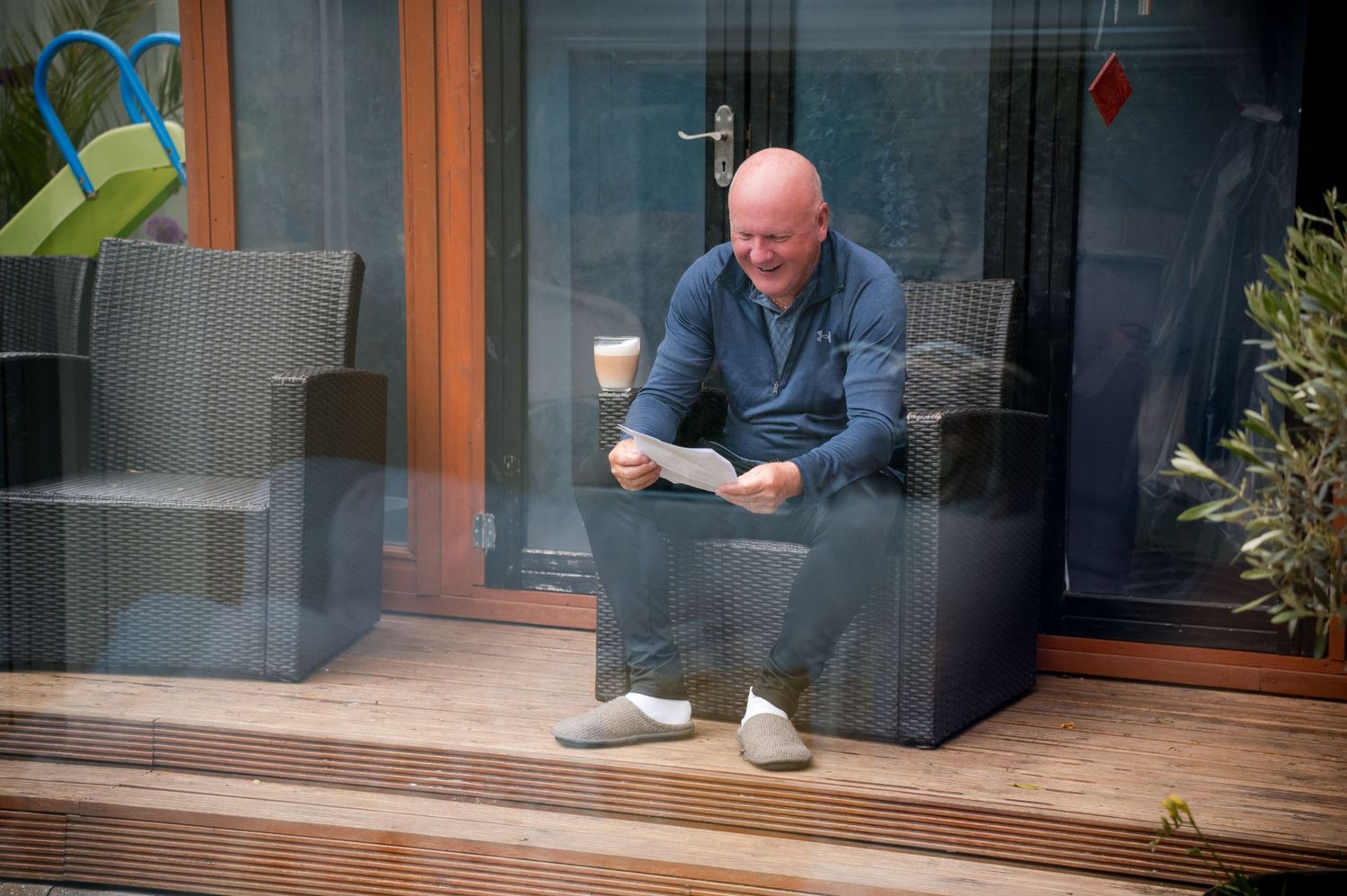 Person in blue shirt crouches down to inspect or repair something near a glass door or window.