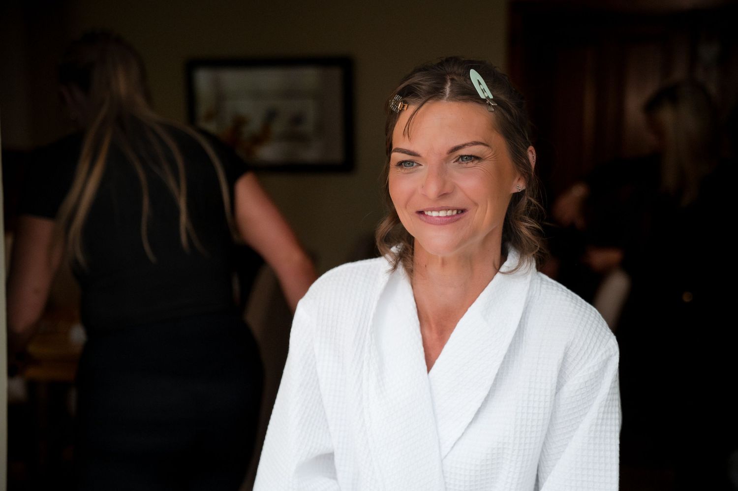 Person wearing a white robe smiles while seated in a dimly lit indoor setting.