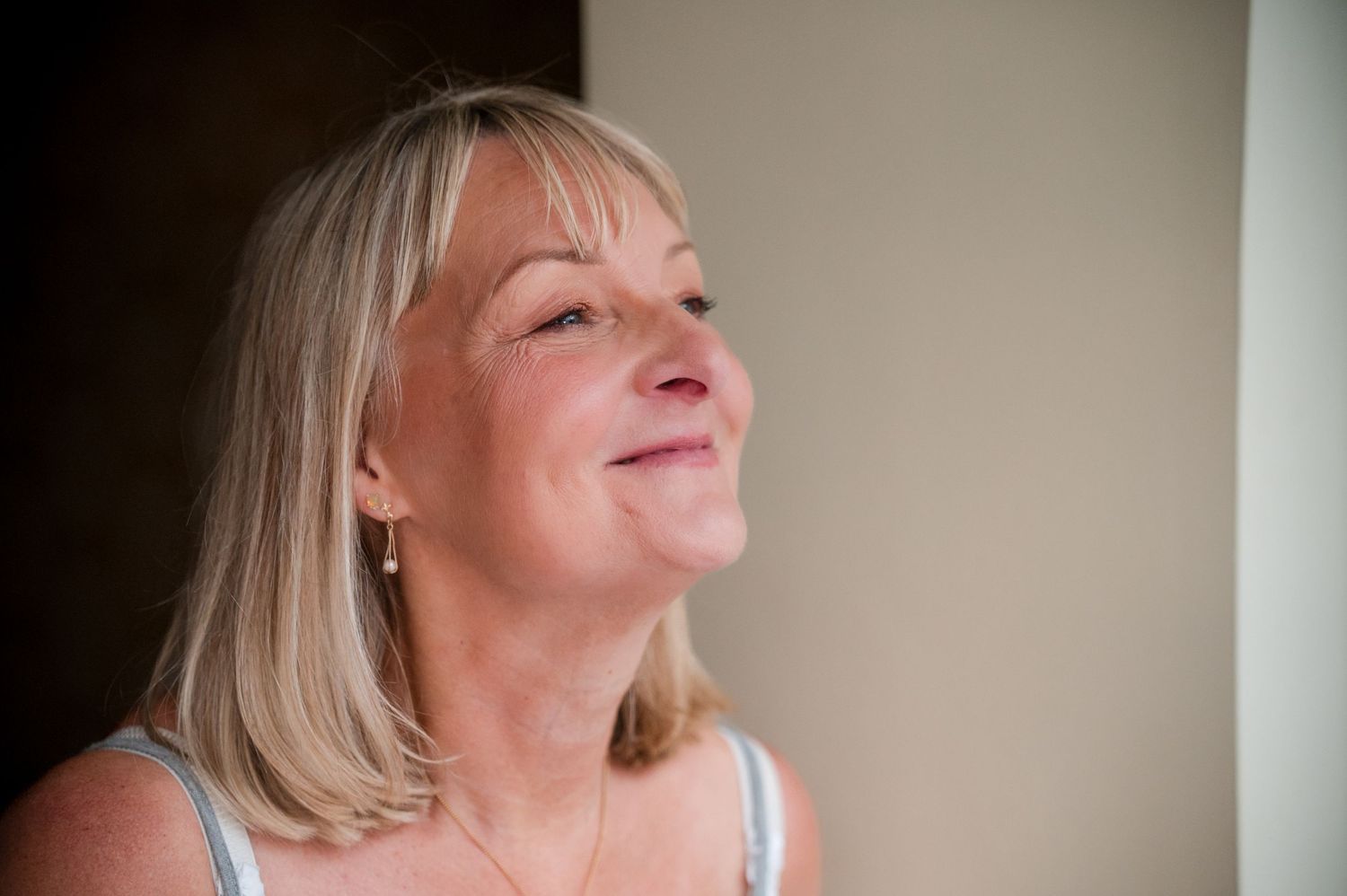 A woman with blonde hair in a white tank top tilts her head back with a serene expression.