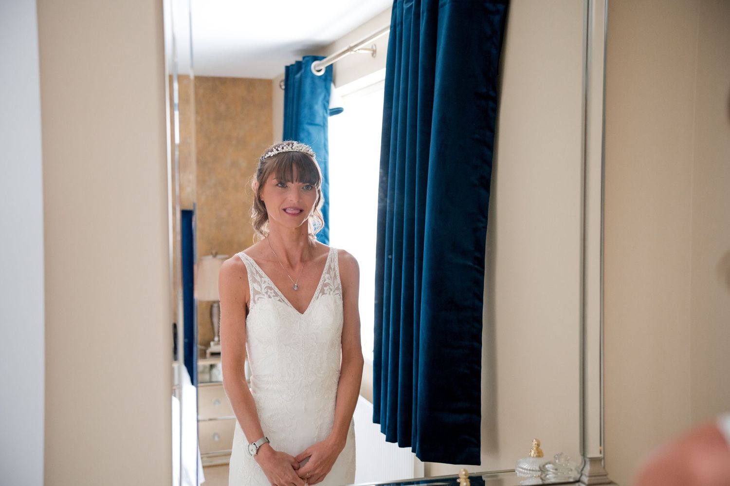 A bride in a white wedding dress stands in a bridal suite while getting ready for her wedding ceremony.