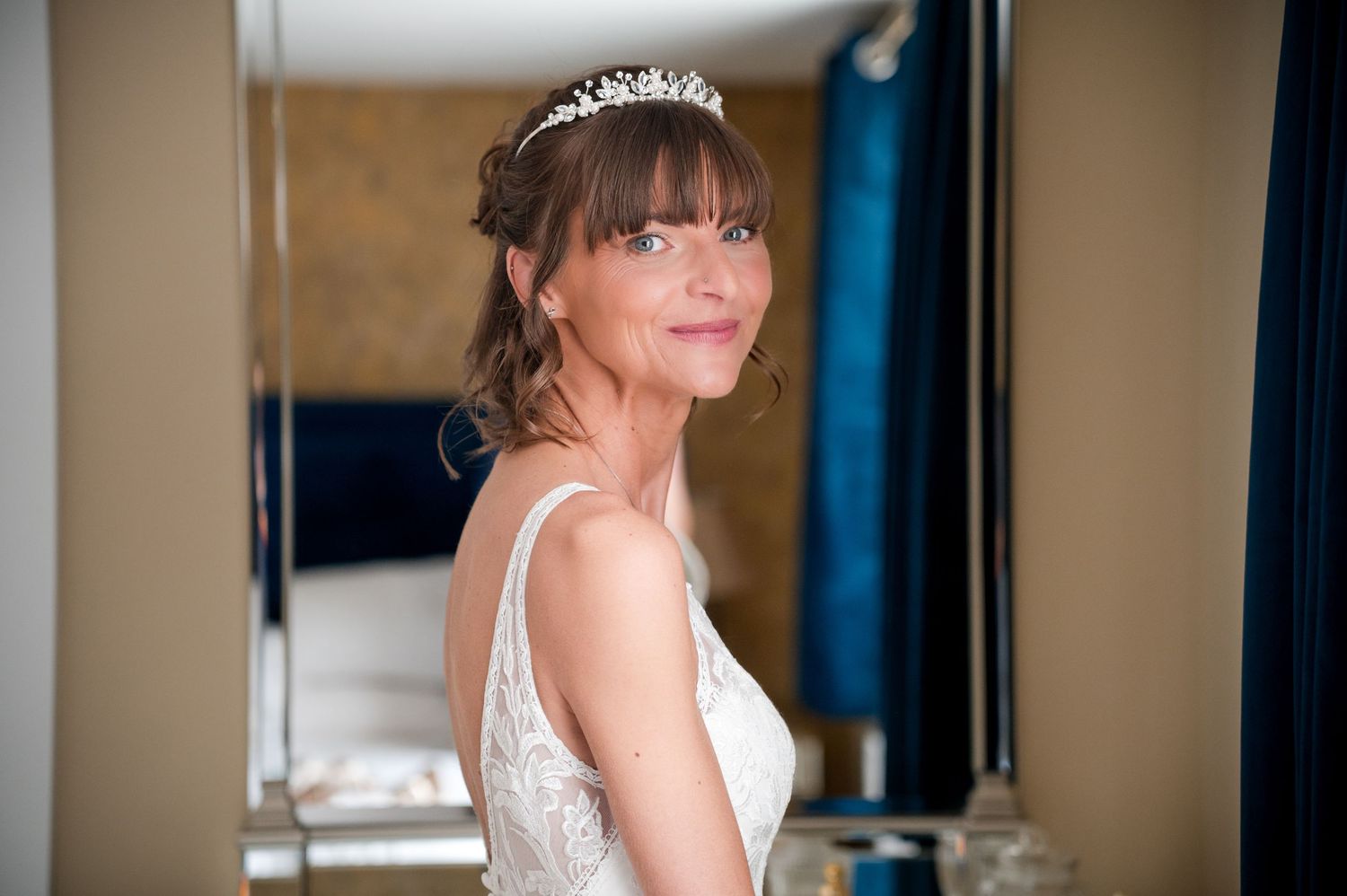 Bride in a white lace dress poses elegantly against a wall with dramatic lighting and shadows.