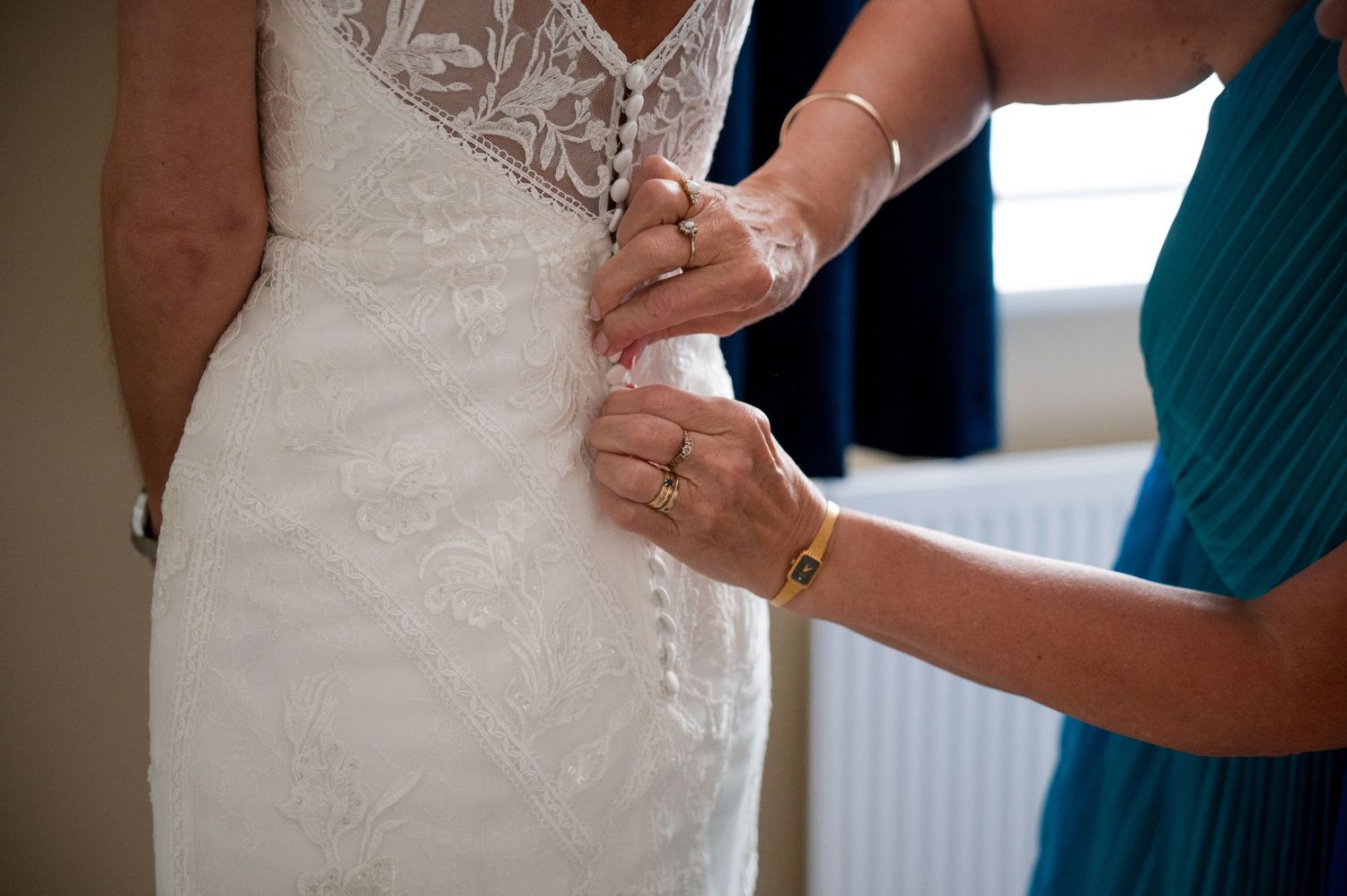Close-up view of hands adjusting a white lace wedding dress with intricate beaded details.