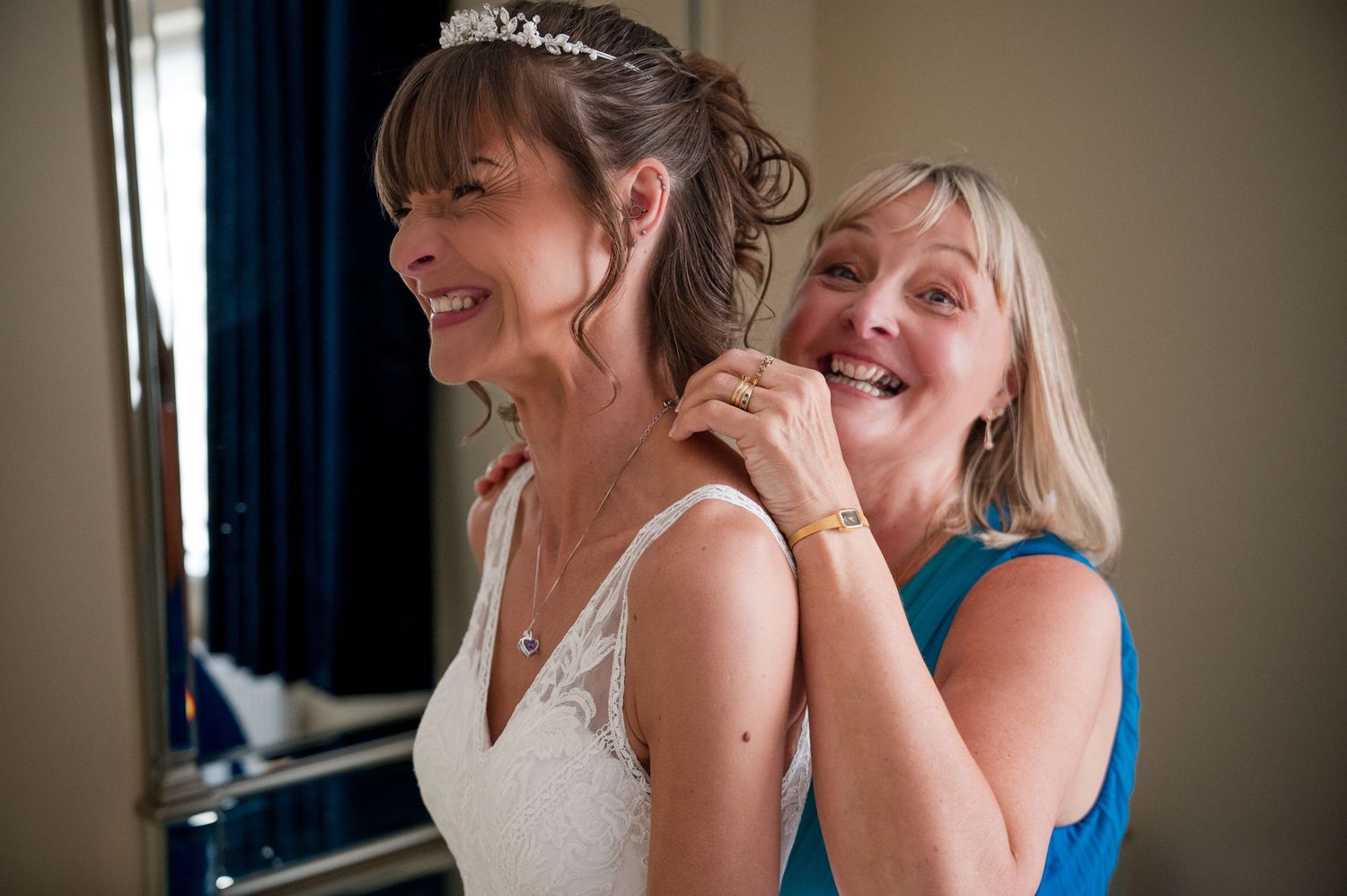 A candid moment of joy and laughter during wedding preparations in a room with blue curtains.