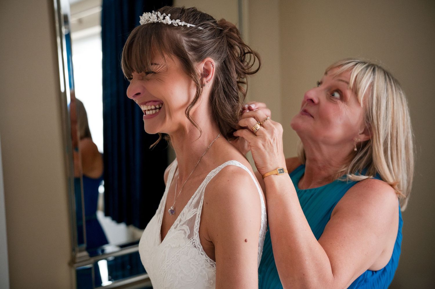 Women in formal dresses and upswept hairstyles laugh together during a celebratory event.