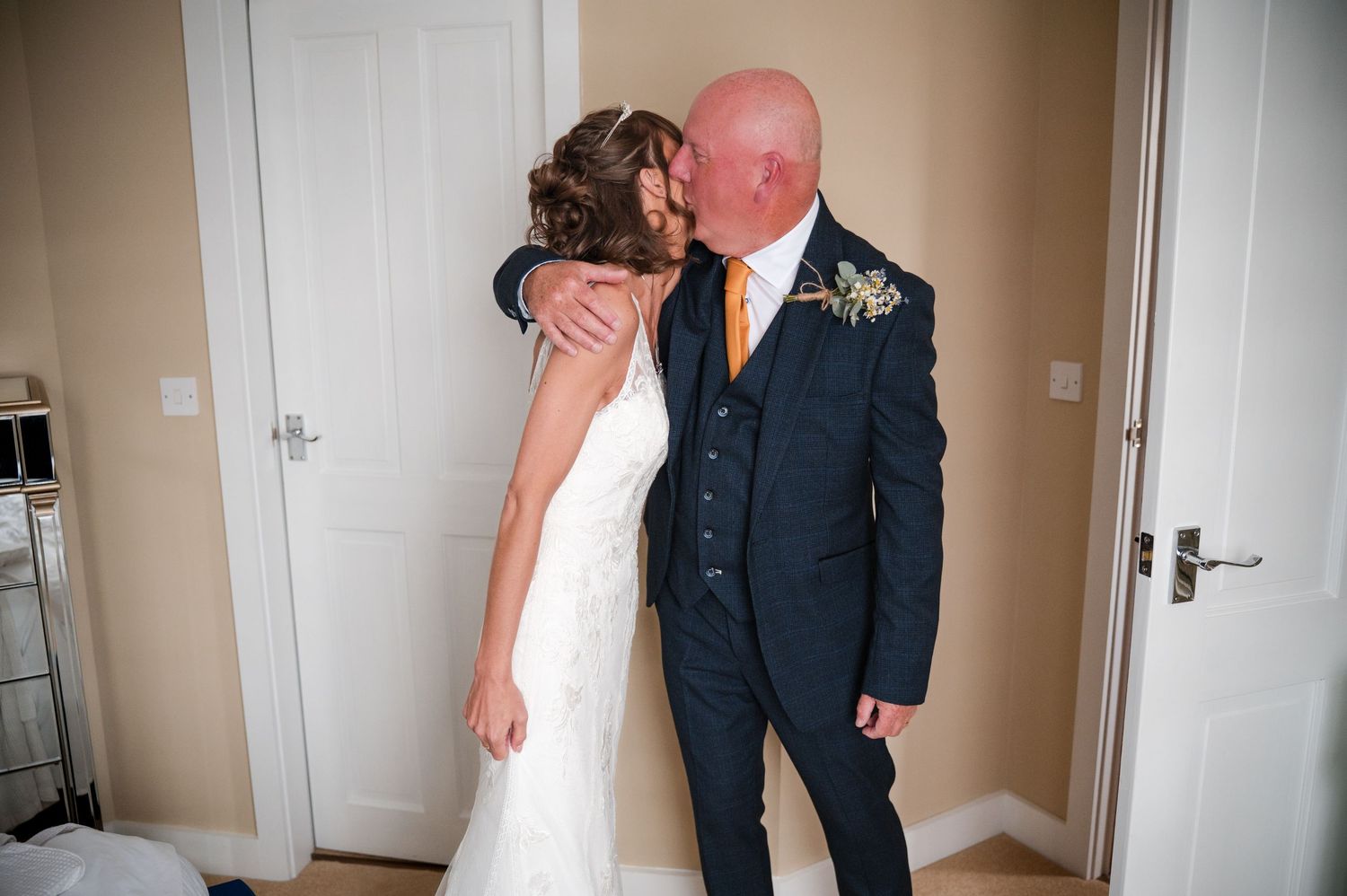 A couple embraces in an intimate moment during their wedding day in a neutral-toned room.