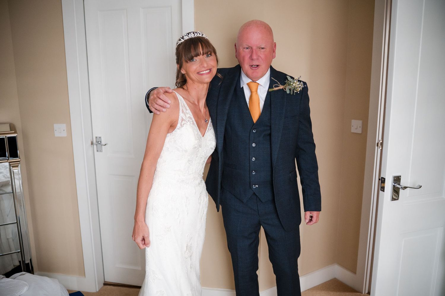 A bride in an elegant white dress stands with a companion in a dark suit during a wedding celebration.