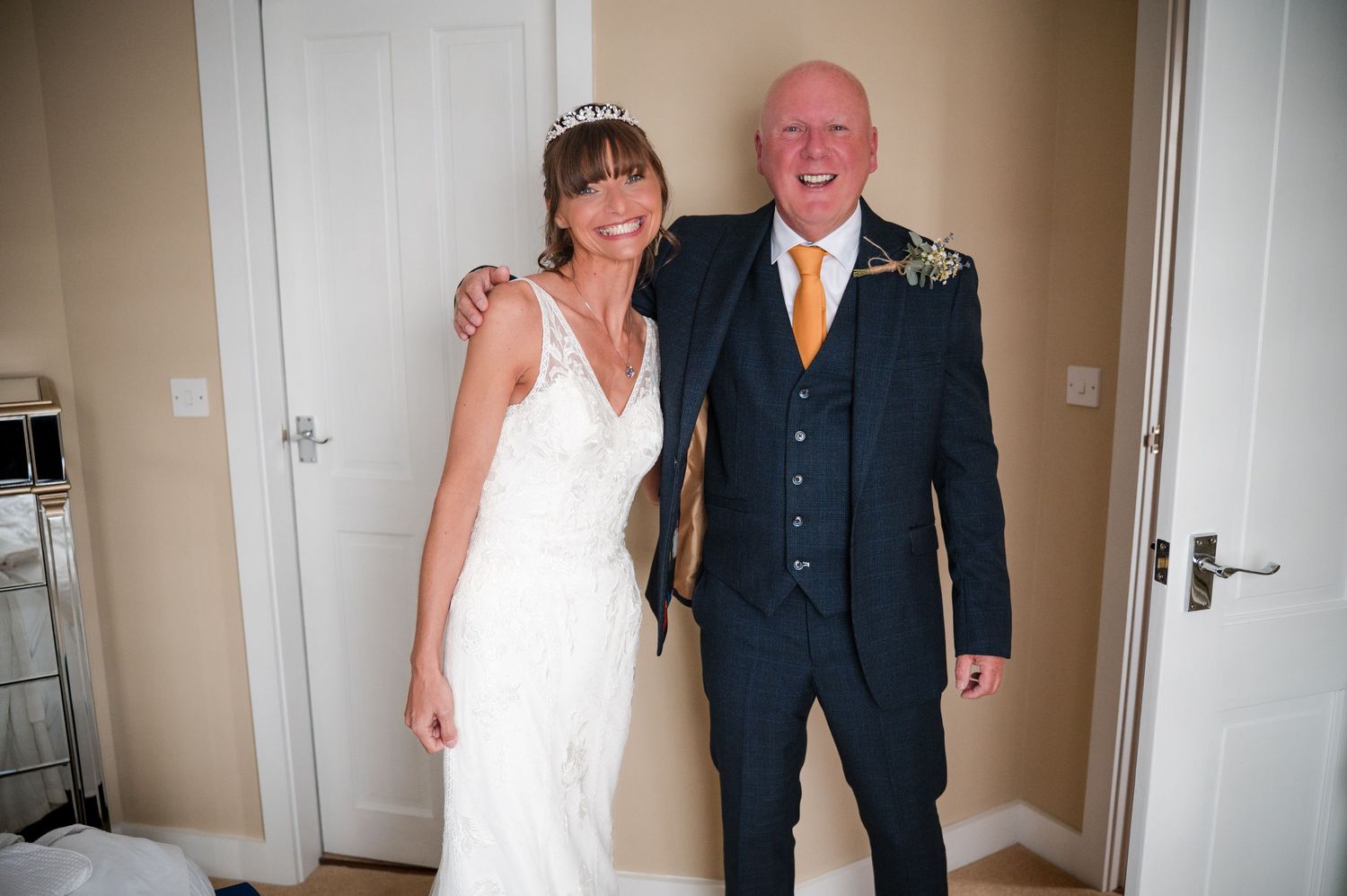 A bride and groom pose together in a hallway wearing traditional wedding attire.