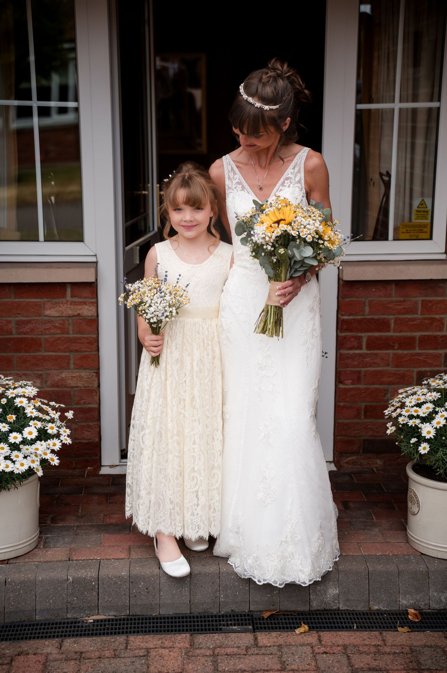 A group in white dresses stand together on a brick porch holding floral bouquets.