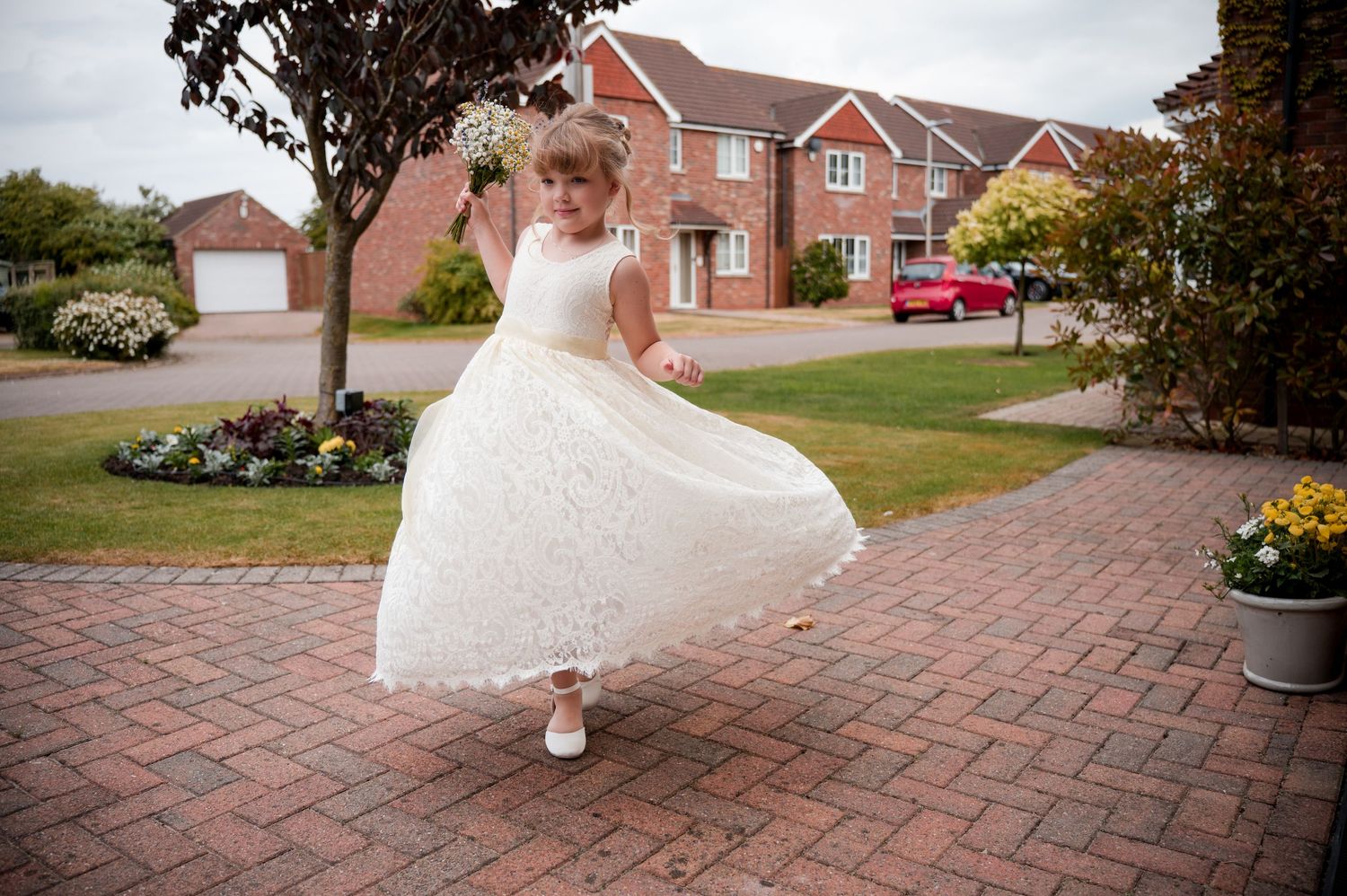 A person in a flowing white wedding dress walks across a brick paved driveway with residential homes in the background.