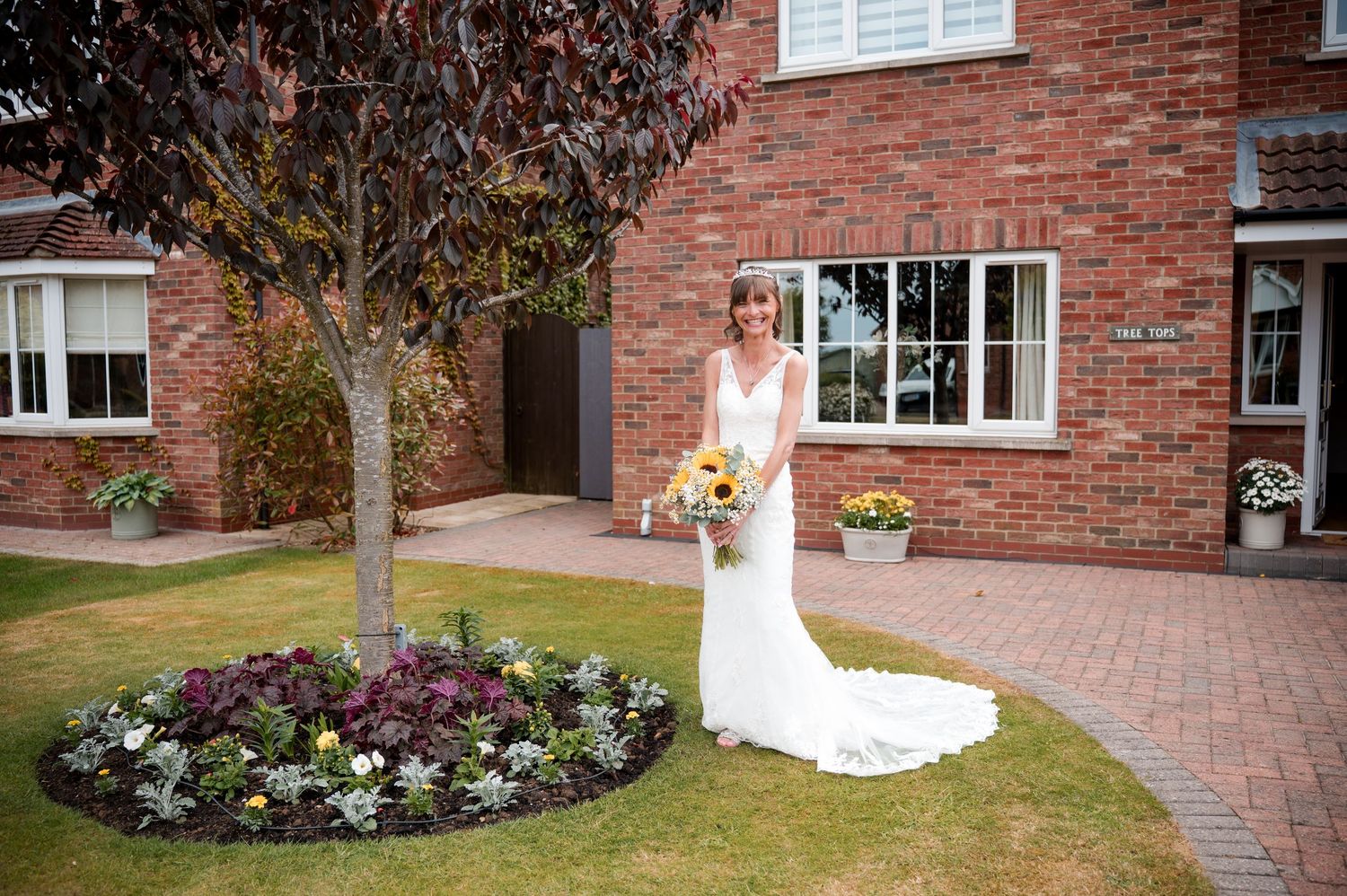 A bride in a flowing white wedding dress poses gracefully in front of a red brick building during a photo session.