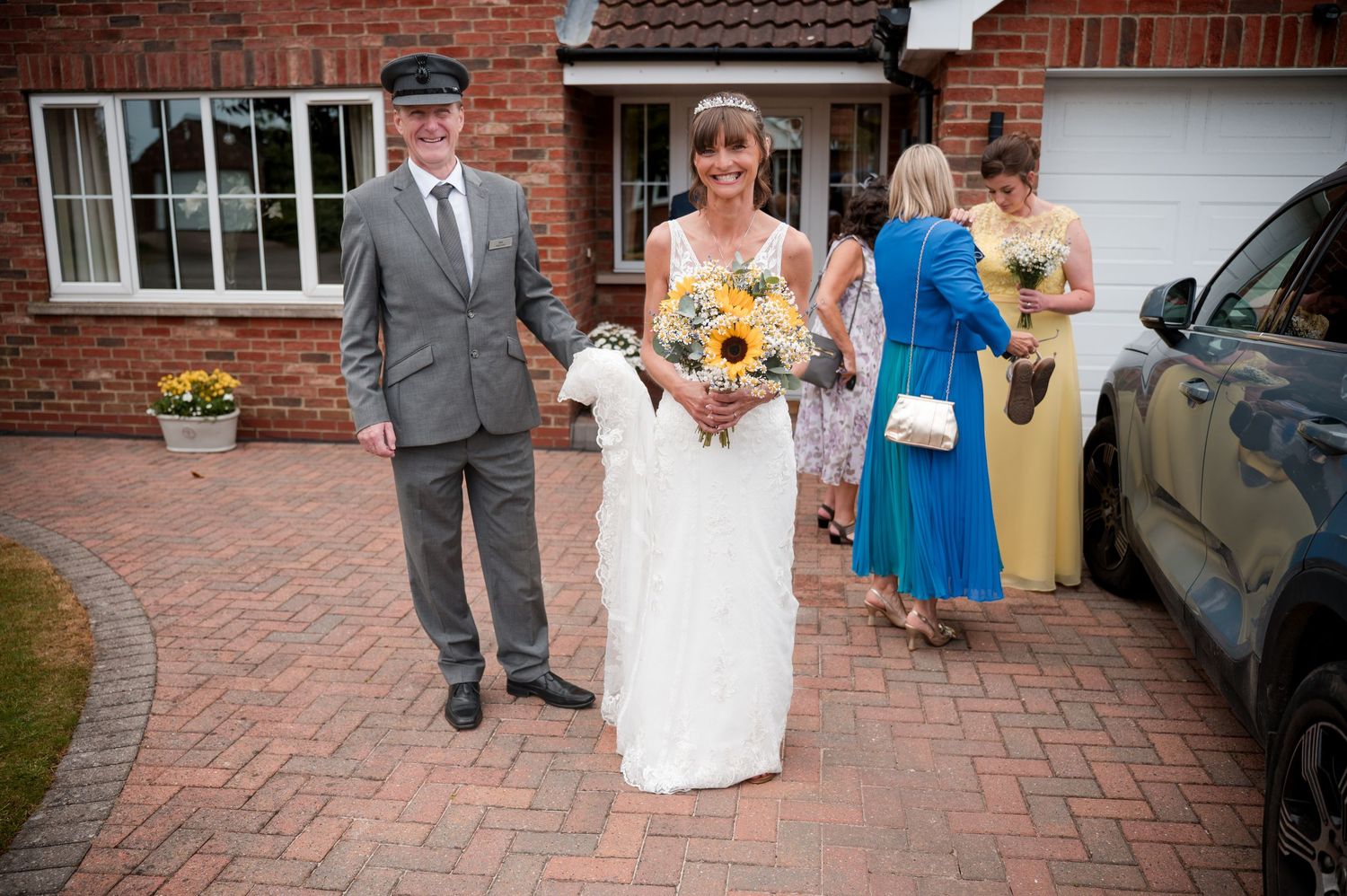 A couple in wedding attire walks together on a brick paved driveway outside a brick building.