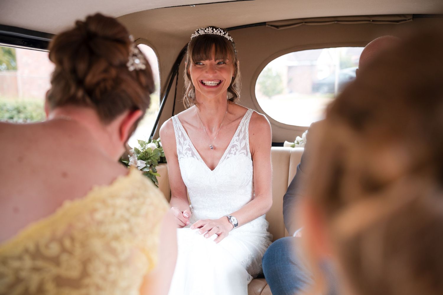 Bride and bridesmaids in white dresses gather together for a candid moment during wedding preparations.