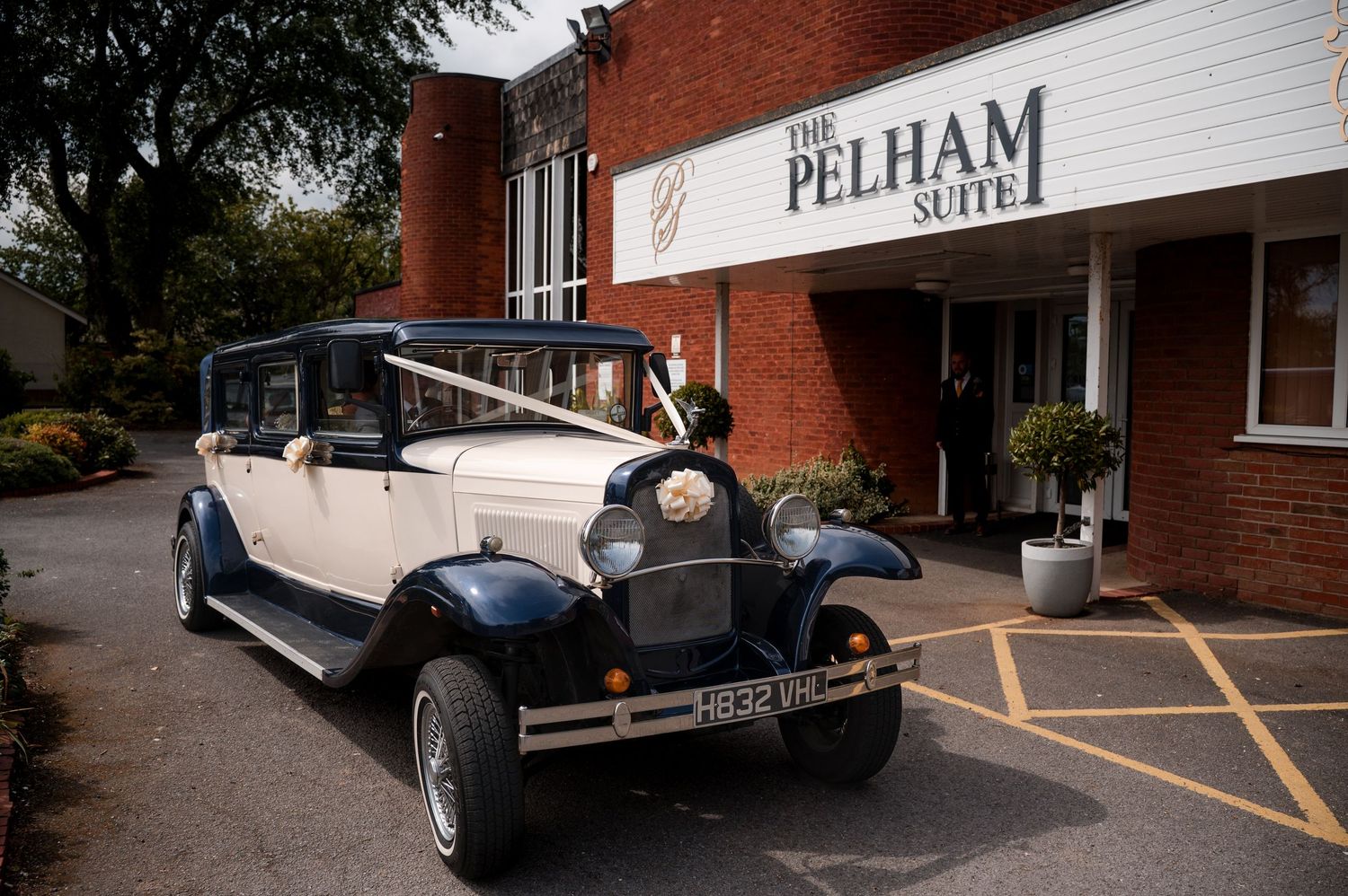 A white Pelham delivery truck parked outside a brick building with vintage cars visible in the scene.