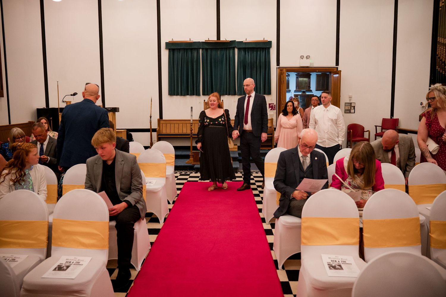 A panoramic view of guests seated in rows at a formal event with white and yellow chair covers.