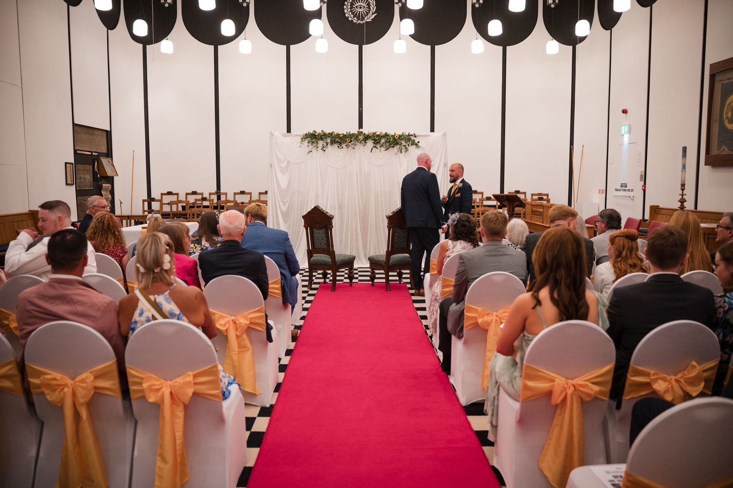 Wedding ceremony venue with rows of chairs decorated with gold sashes and a red carpet aisle runner.