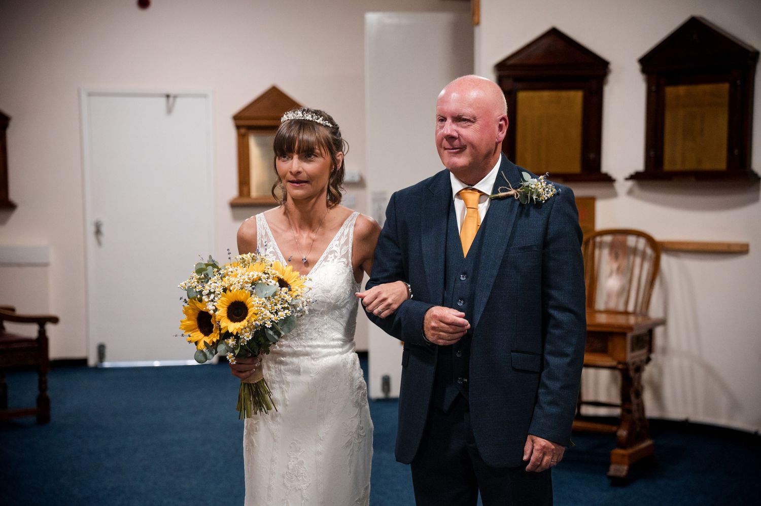 Wedding guests enjoying a candid moment at a rustic indoor reception venue decorated with sunflowers.