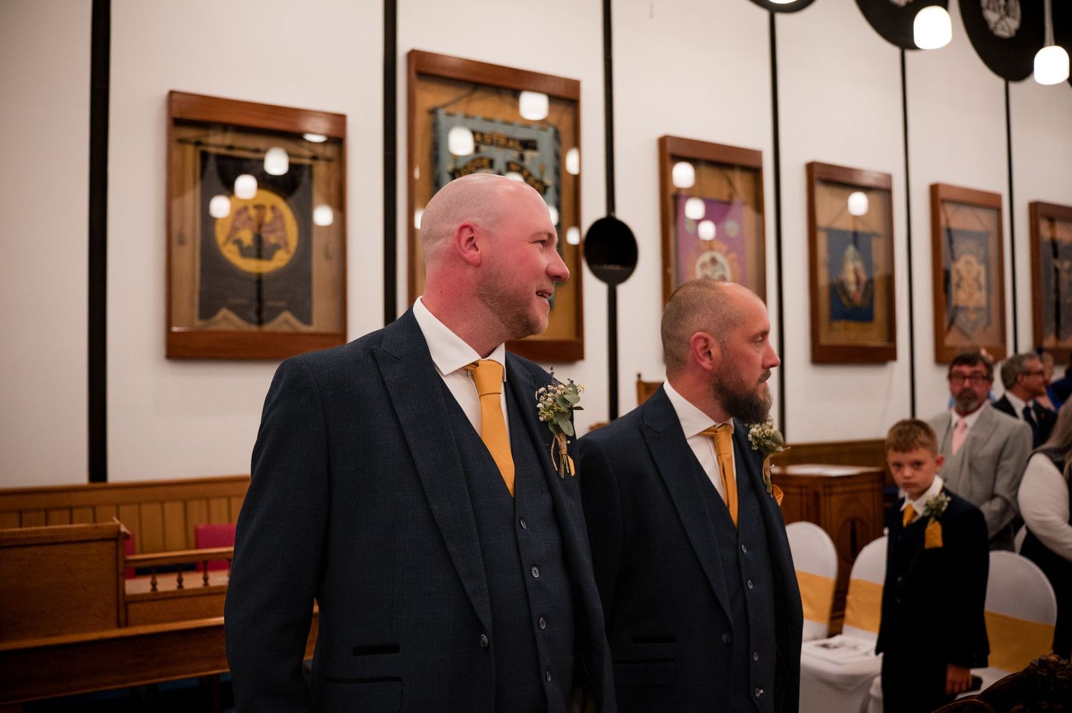 A panoramic view of well-dressed people in formal attire standing in an elegant wood-paneled hallway with framed artwork.