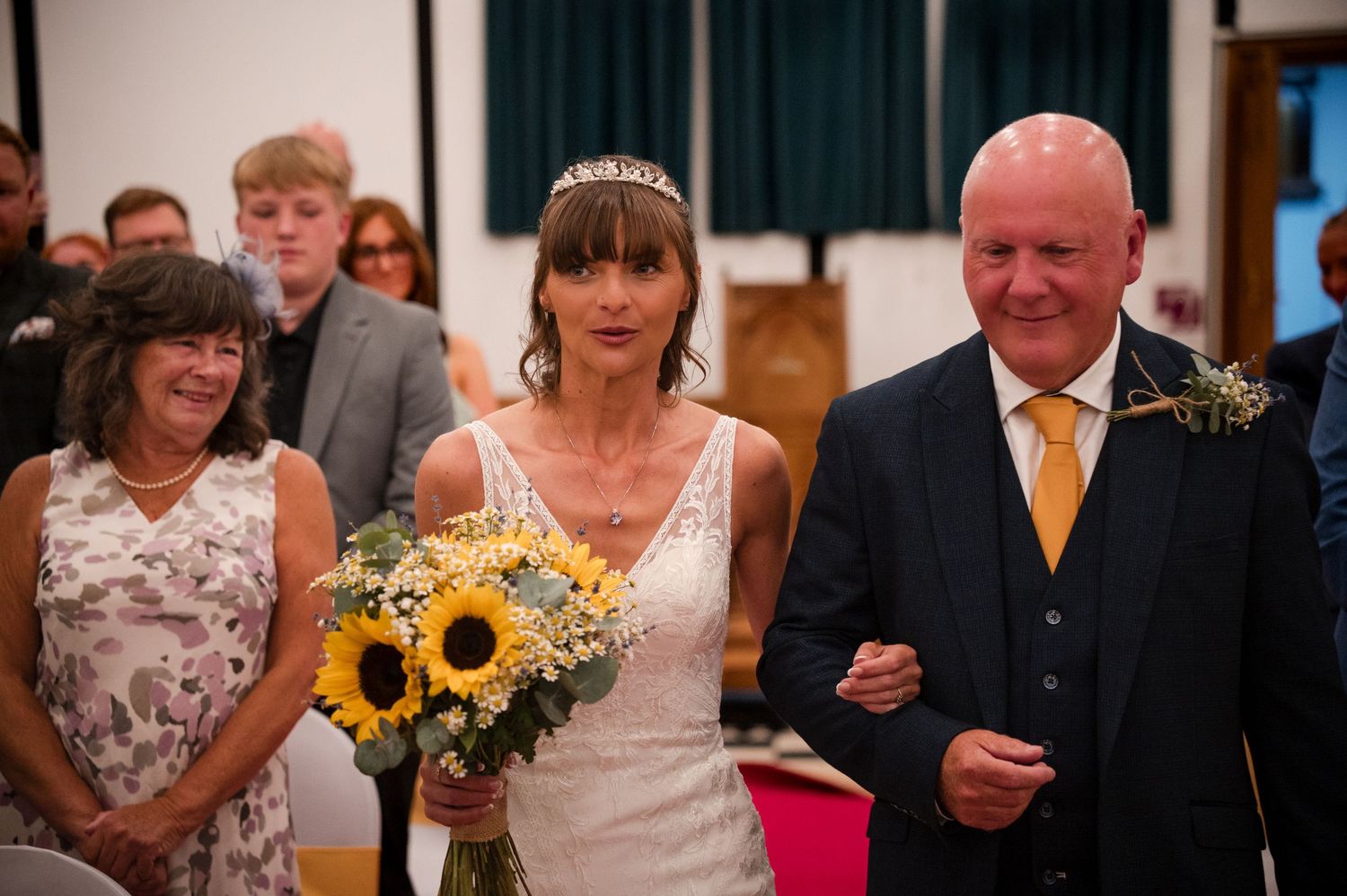 Wedding guests smile and celebrate during an indoor reception with sunflowers and floral decorations.