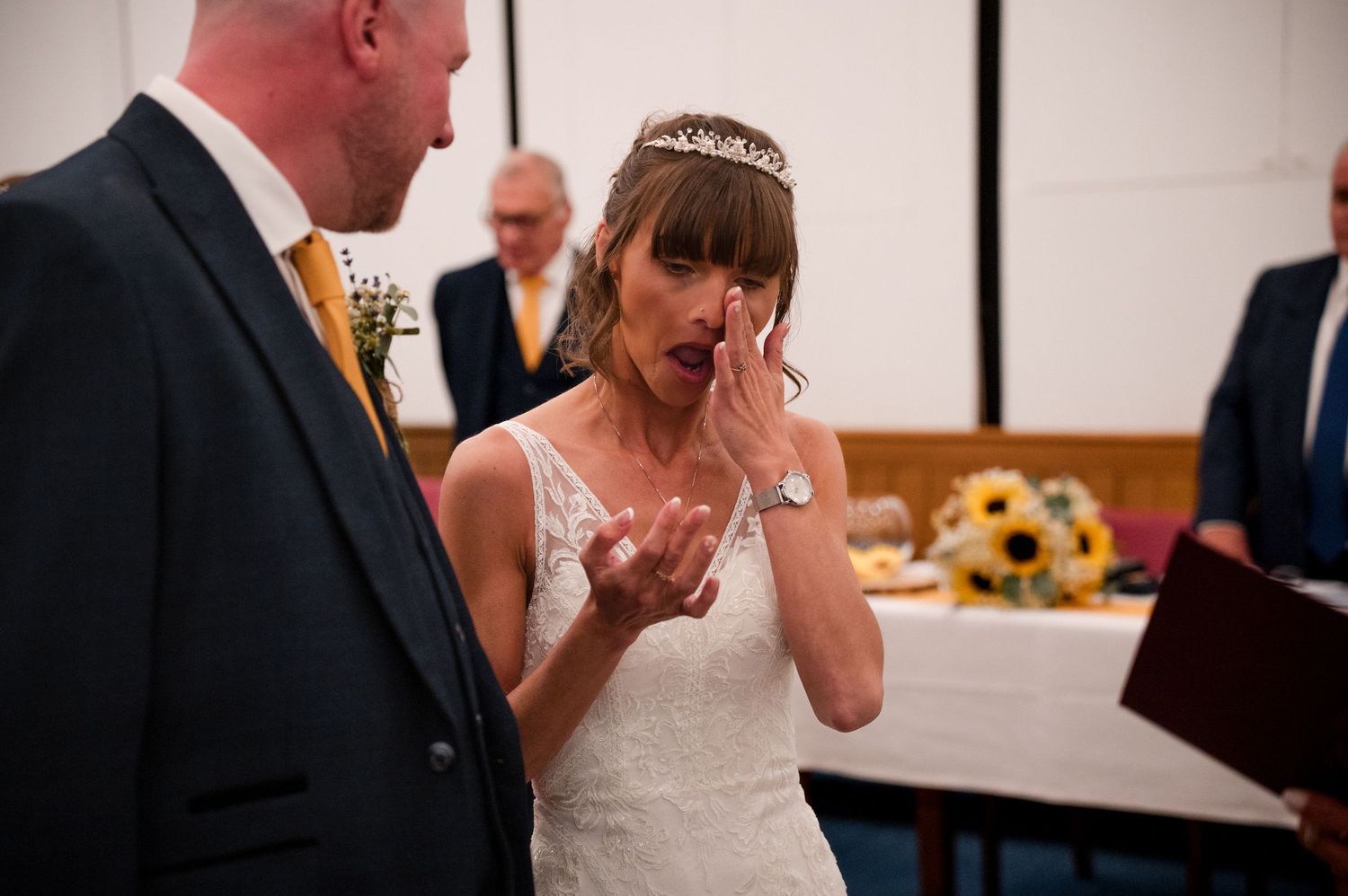 Emotional reactions during a wedding ceremony as bride wipes away tears while wearing a white gown and tiara.