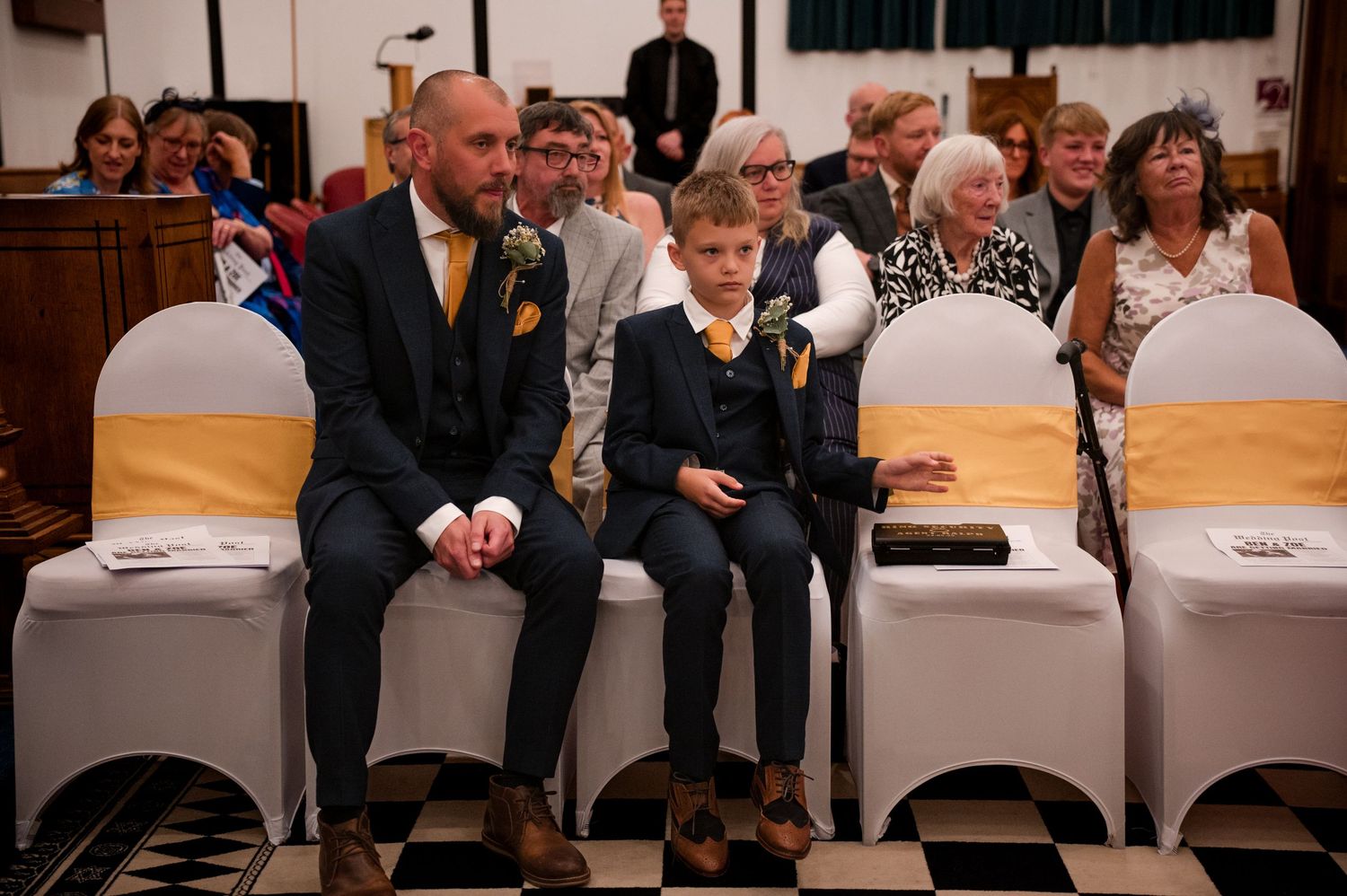 People sitting in rows of chairs with white covers at what appears to be a formal event or ceremony.