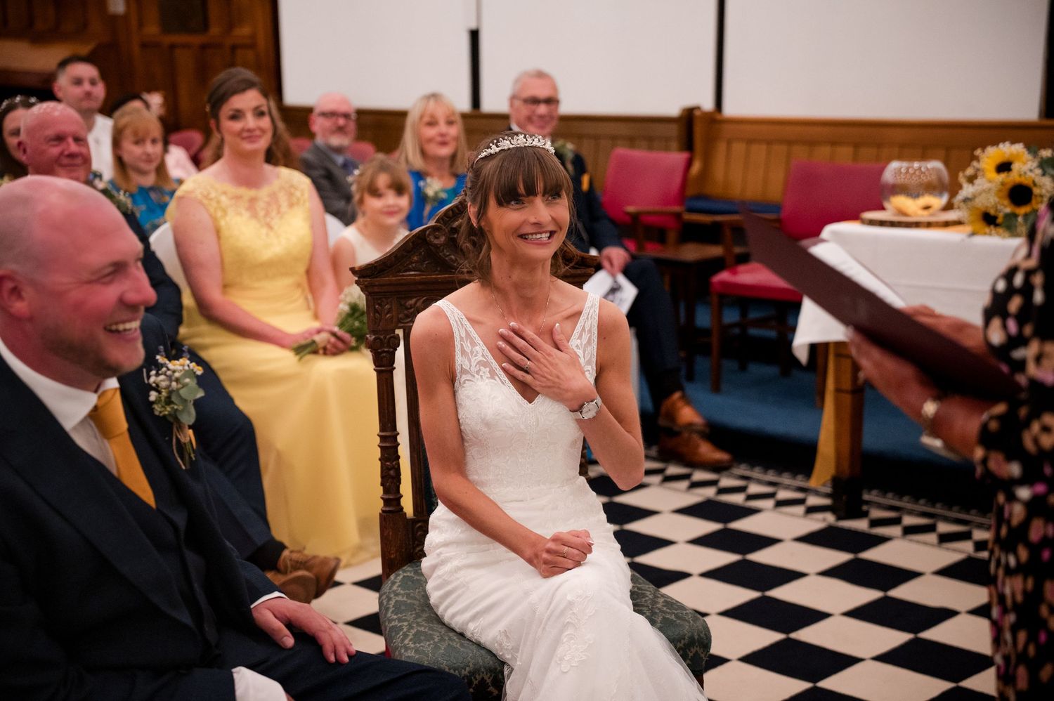 Wedding guests seated in a church with black and white checkered floor during an emotional ceremony moment.