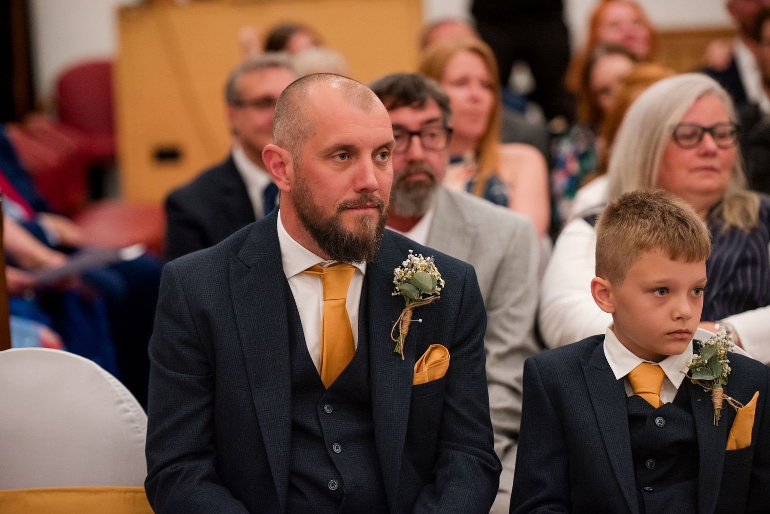 Wedding party members in black suits with orange accents stand together during a formal ceremony.