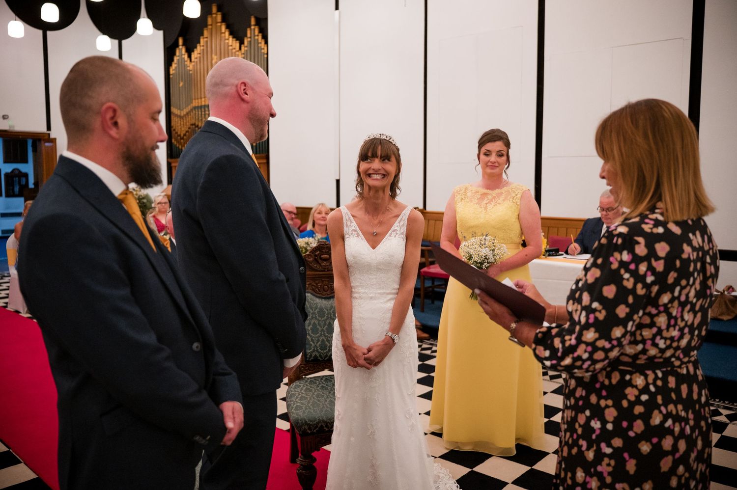 A wedding ceremony takes place on a black and white checkered floor with people gathered for the special moment.