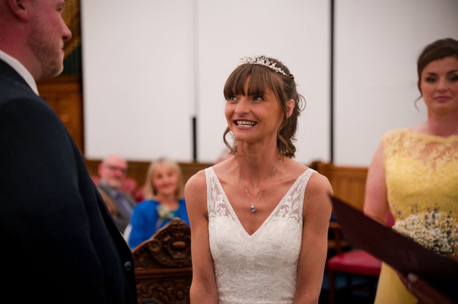 A bride in a white lace wedding dress smiles during a reception celebration.