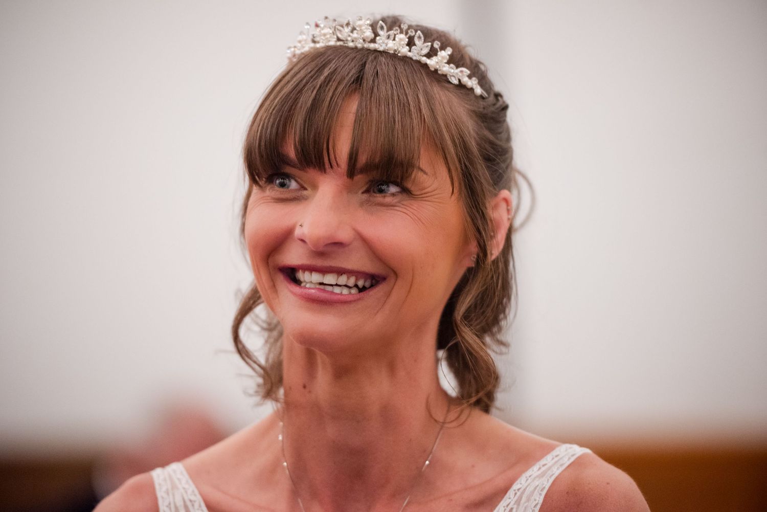 A bride in a white dress and tiara poses with a joyful expression during her wedding celebration.