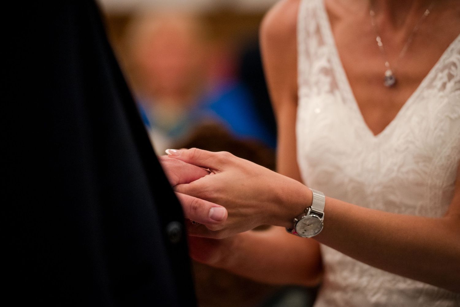 Close-up of hands exchanging wedding rings during a marriage ceremony, with bride wearing white lace dress.