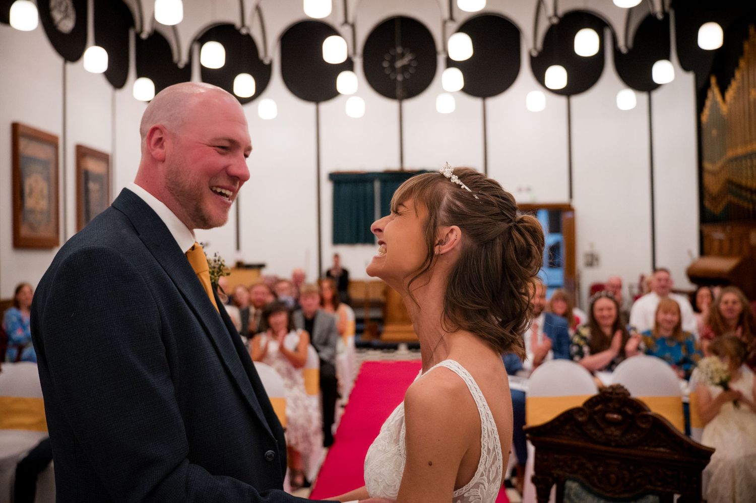 A couple shares a joyful moment during their wedding ceremony under decorative white lanterns with guests looking on.
