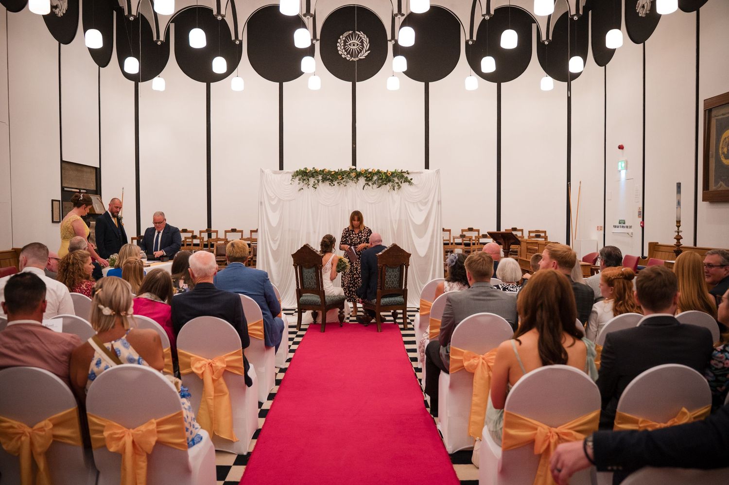 Wedding reception hall decorated with orange chairs and hanging black vinyl records as ceiling decor.