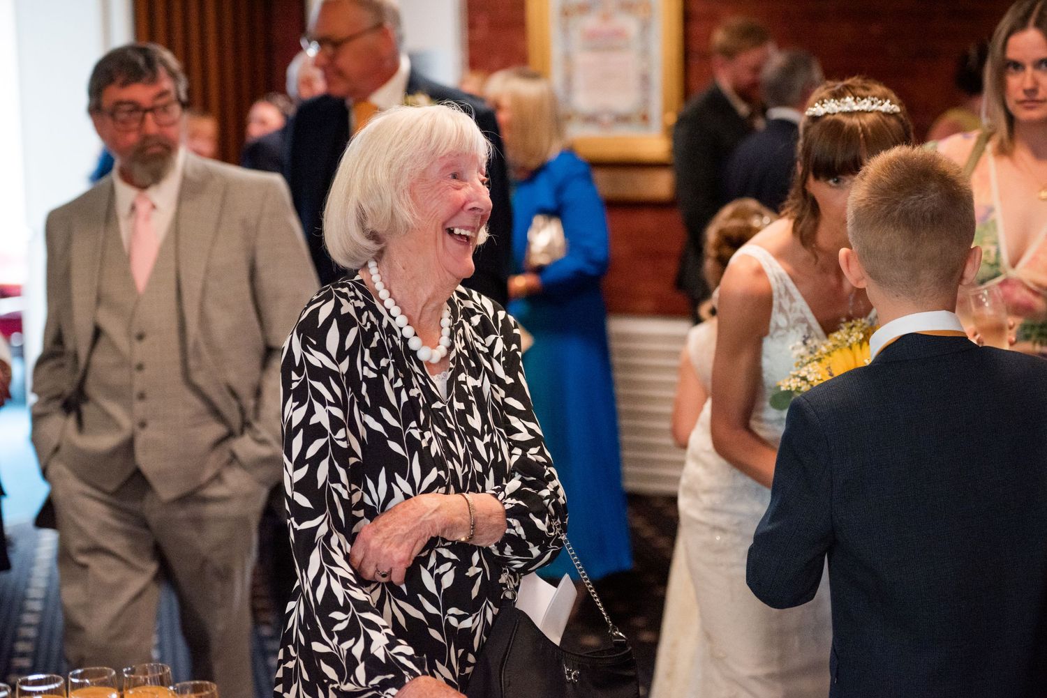A woman in a black and white patterned dress laughs joyfully during a wedding reception celebration.