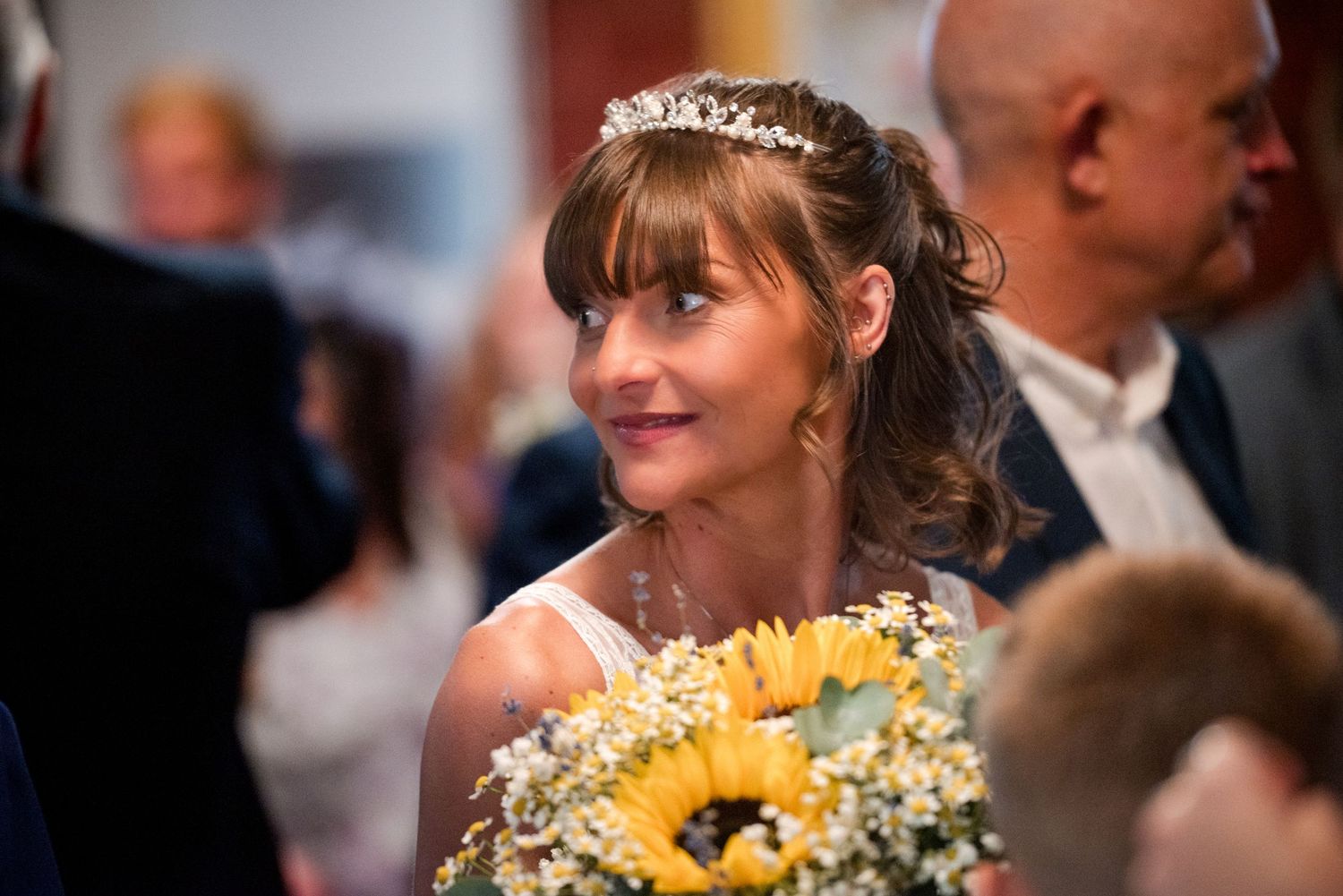 Wedding party walking down a hallway with brick walls and patterned carpet carrying yellow sunflower bouquets.