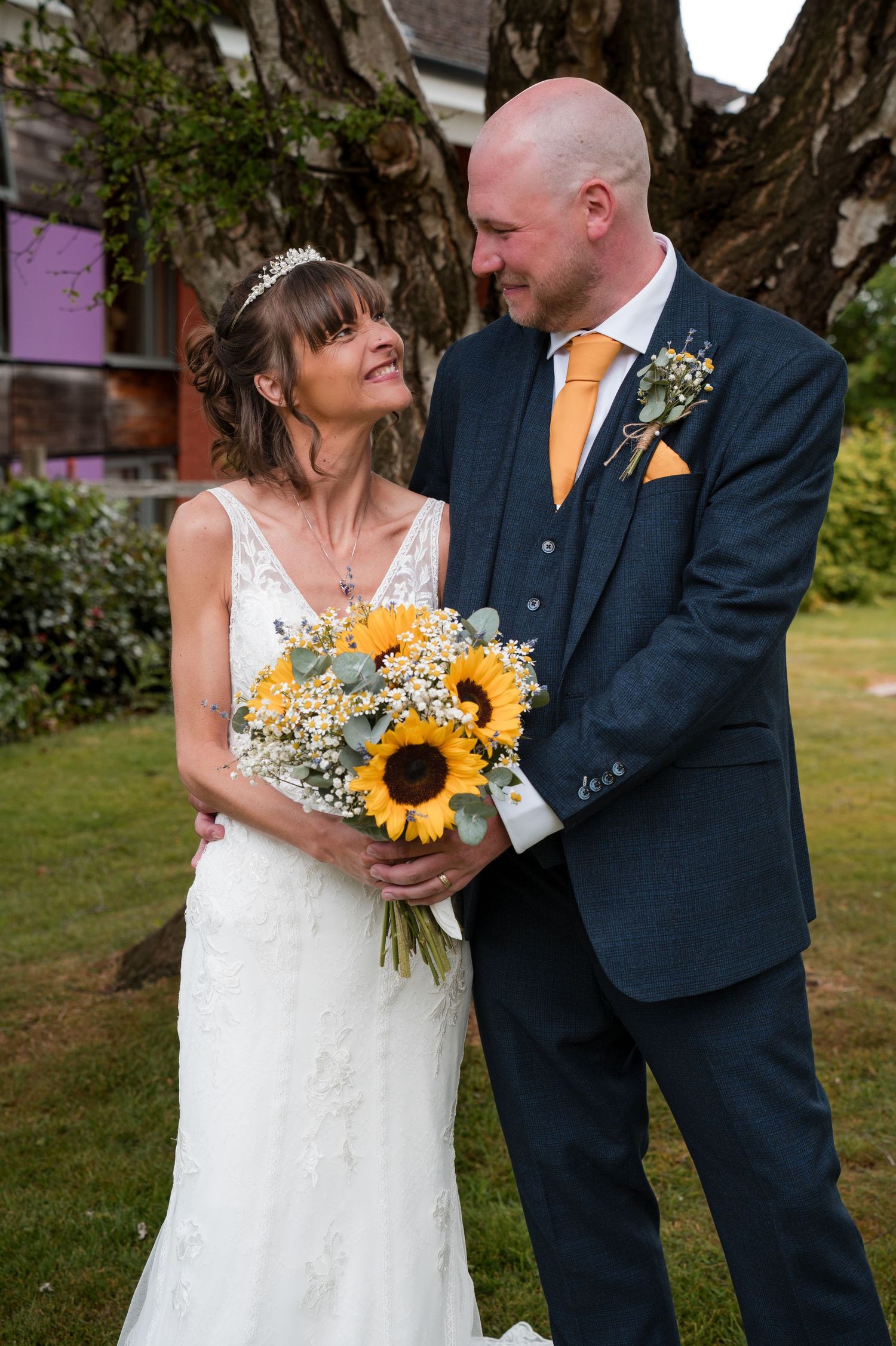 Newlywed couple shares joyful moments outdoors with vibrant sunflower bouquet and baby's breath florals.