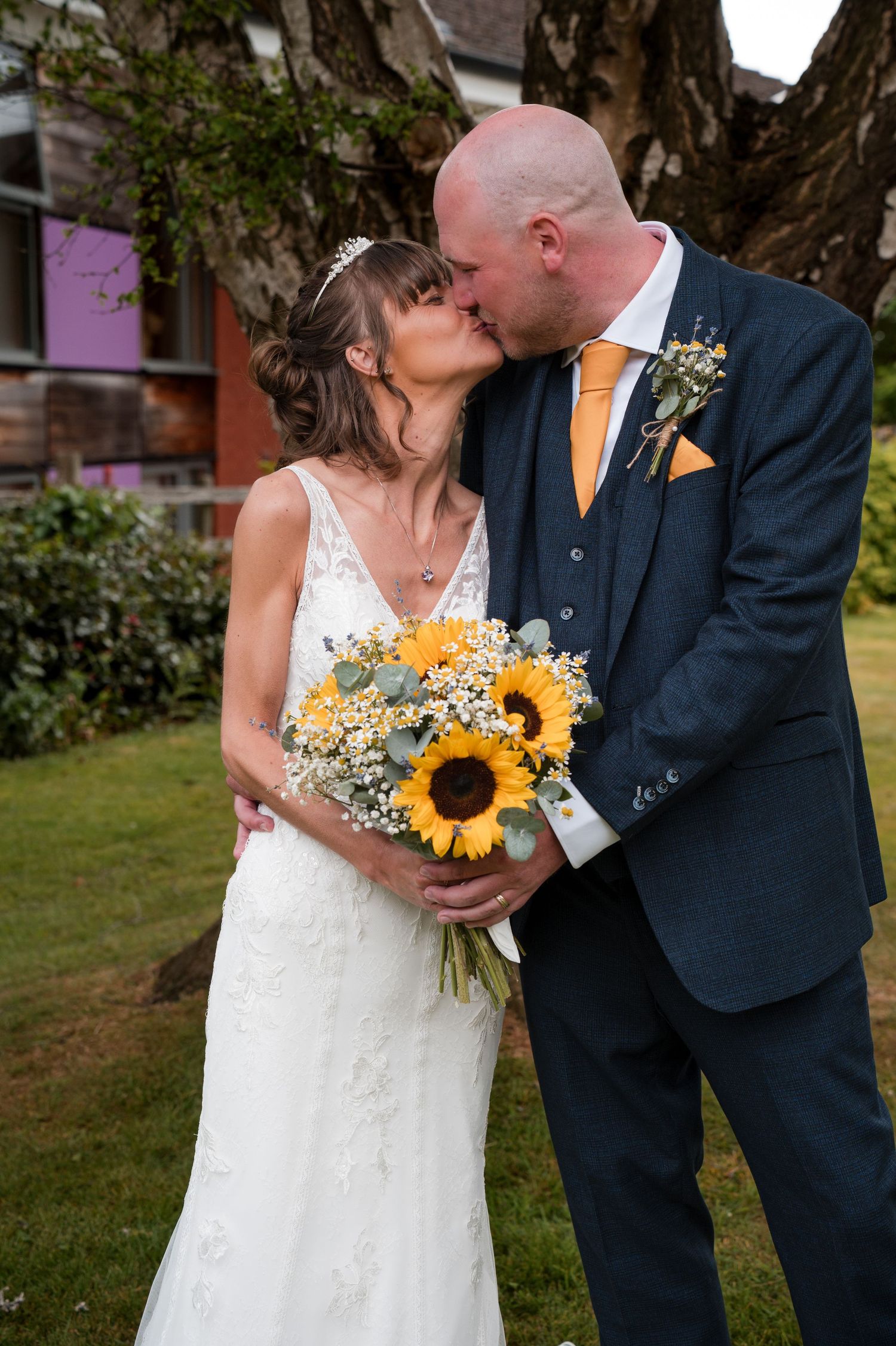 A romantic wedding couple shares tender kisses while the bride holds a vibrant sunflower and baby's breath bouquet.
