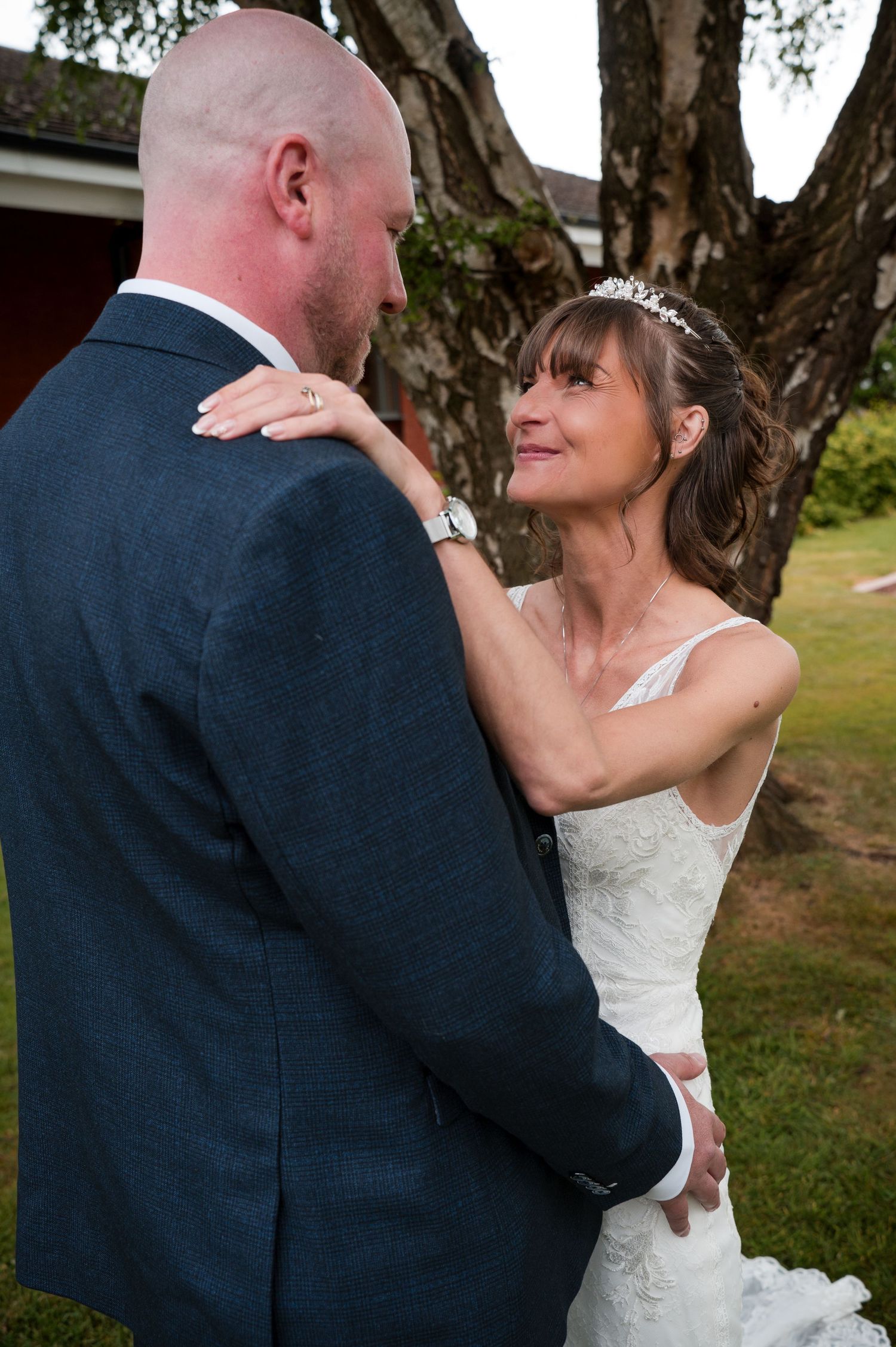 A couple in wedding attire share an intimate dance moment outdoors under a tree.