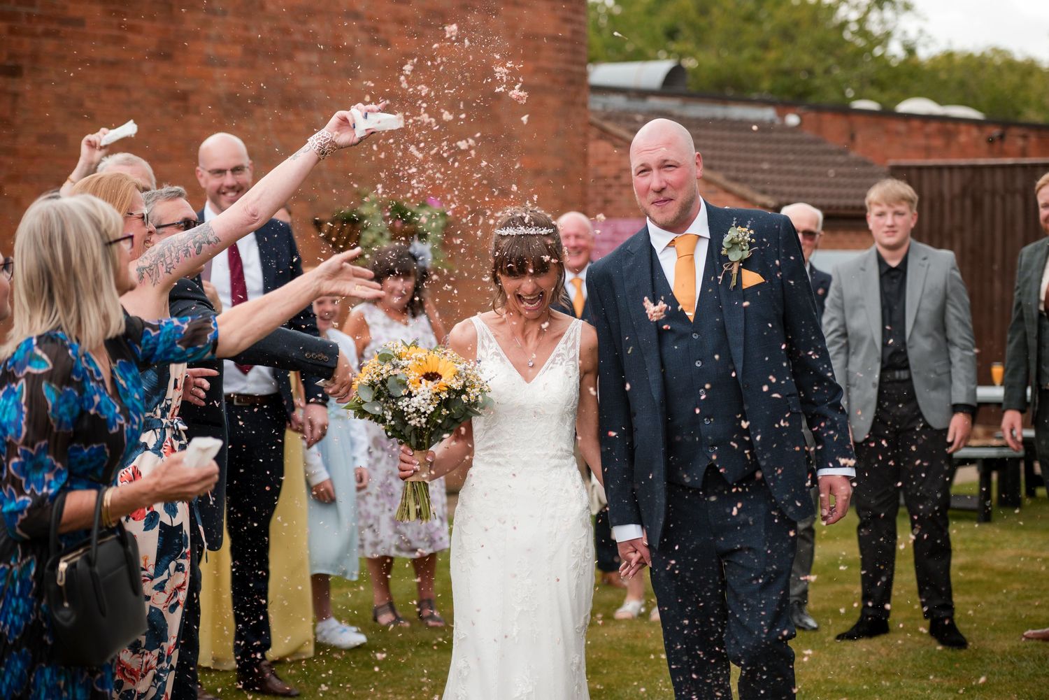 Wedding party stands in a line while guests throw confetti during an outdoor celebration.